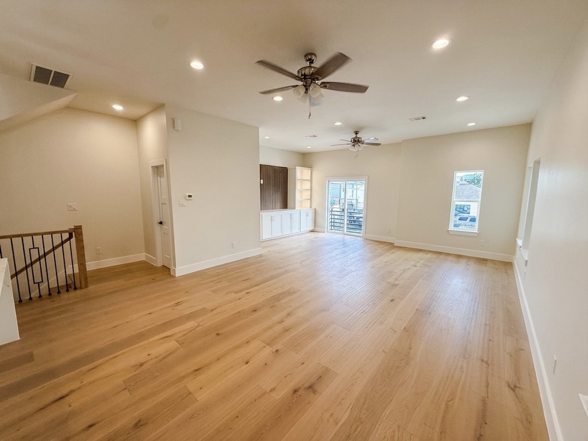 Spacious open living area with sleek hardwood floors, recessed lighting, and ceiling fans, leading to a bright space with large windows and double doors opening to a small patio on 2nd floor.