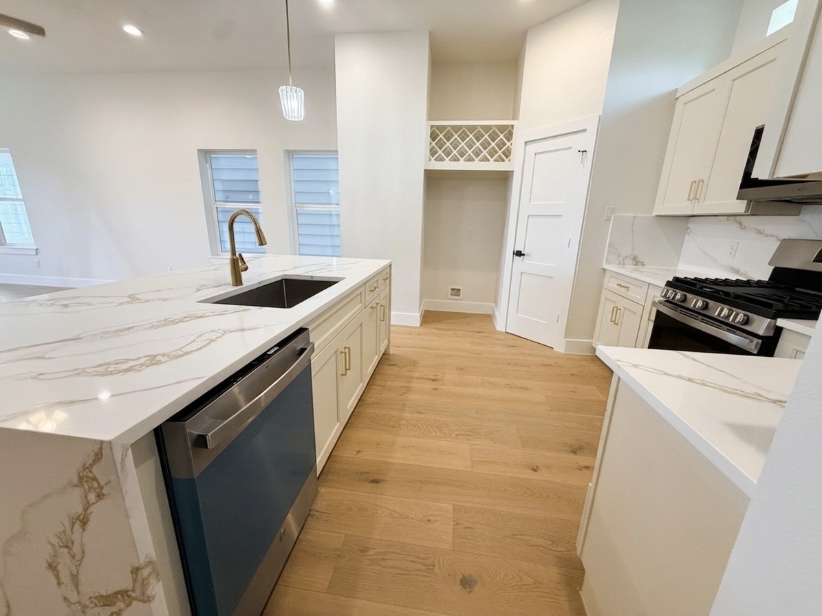 Elegant kitchen featuring sleek quartz countertops, modern stainless steel appliances, and light engineered wood flooring.
