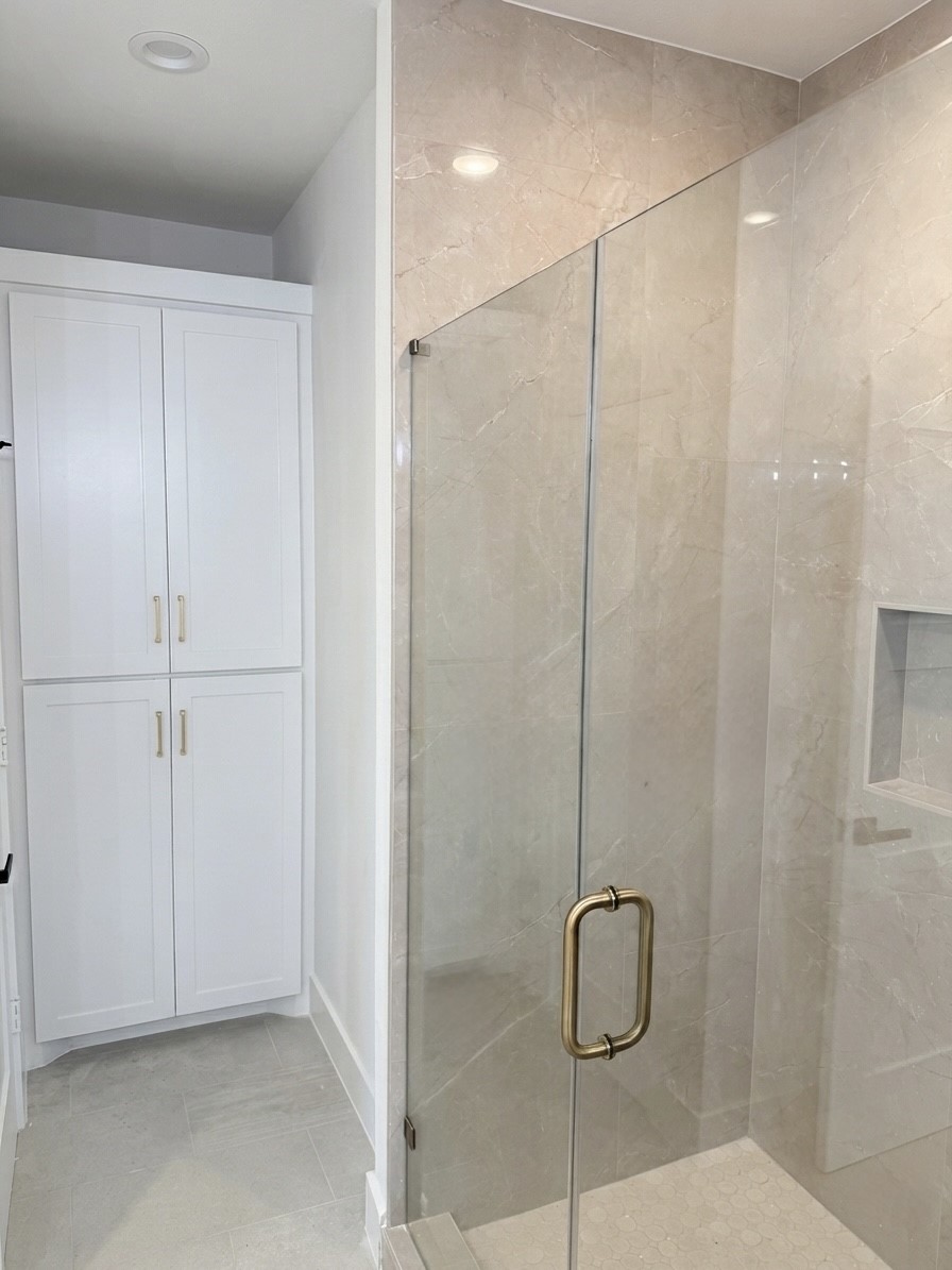 Elegant bathroom featuring a spacious glass-enclosed shower with stylish tile work and ample storage in the sleek white cabinetry.