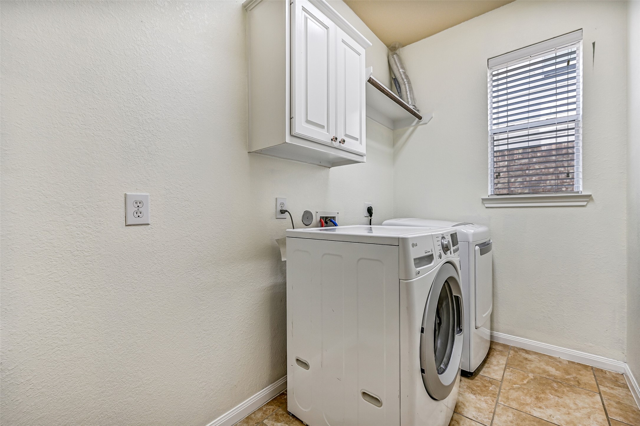 Conveniently located on the first floor, the utility room offers tile flooring, upper storage cabinetry, and a built-in shelf for laundry essentials. A window provides natural light to brighten daily chores, while additional floor space allows room for a bonus refrigerator or freezer, keeping extra storage conveniently tucked away from the main living areas.