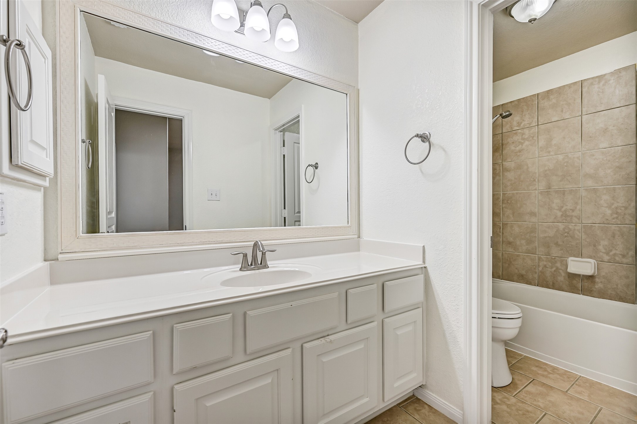 This Jack & Jill style bathroom serves the adjoining secondary bedrooms and is thoughtfully designed with separate vanity and bathing areas for added functionality. Features include a lengthy cultured marble countertop with an undermount basin sink, a seated makeup vanity with lap drawer, white cabinetry, updated lighting, tile floors, and a private combination bathtub and shower with a tile surround.