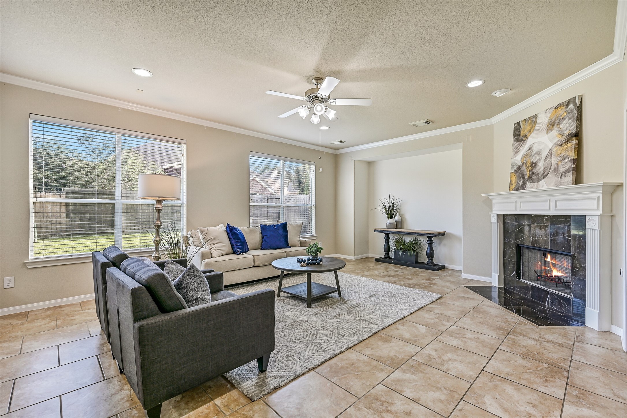 The spacious family room serves as the centerpiece of the home, offering generous space for everyday living and entertaining. Large rear-facing windows fill the room with natural light, while crown molding, recessed lighting, a ceiling fan, and easy-maintenance tile flooring create a comfortable and inviting atmosphere.