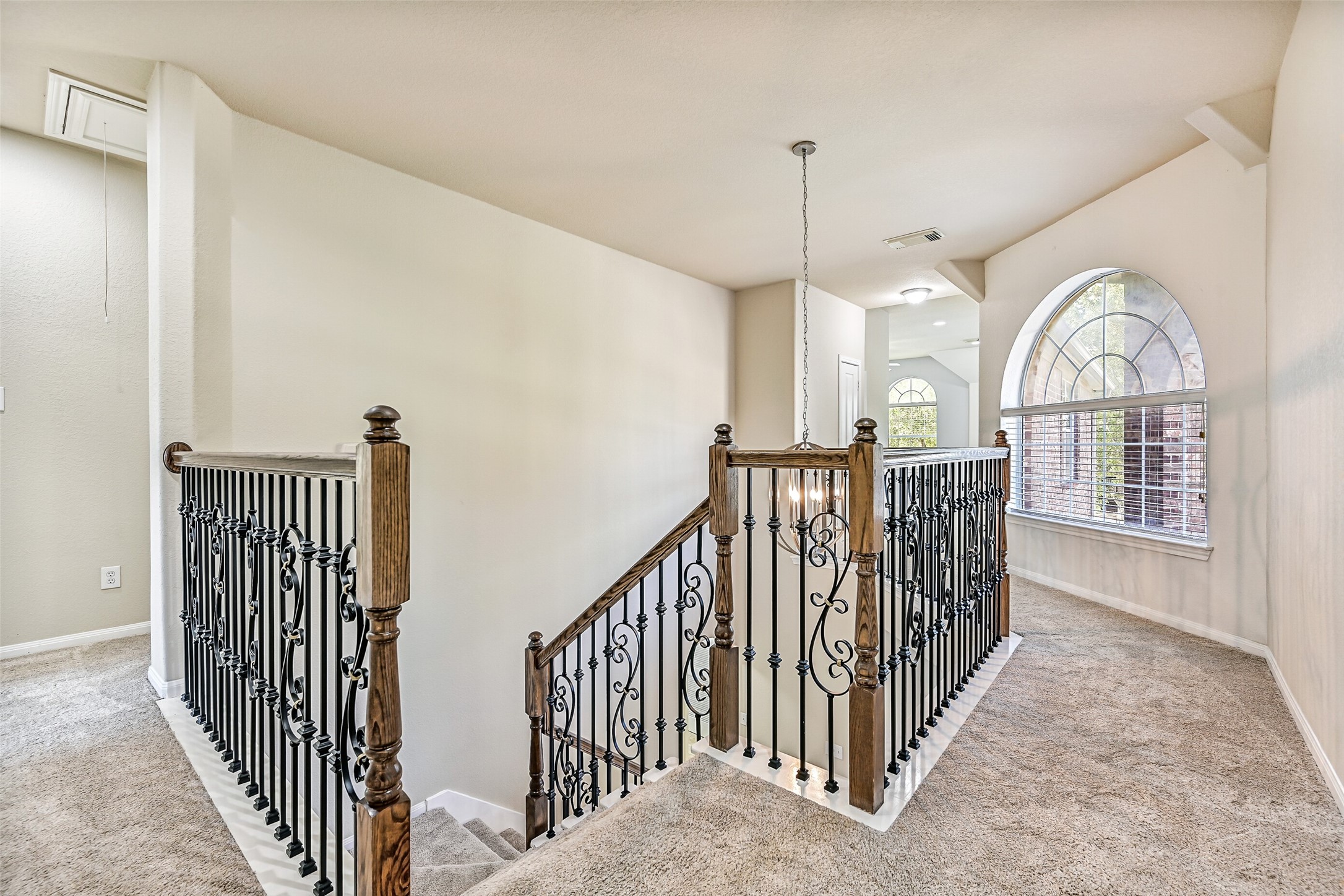 Ascend the sweeping split staircase to an impressive second-floor overlook featuring plush new carpet, decorative wrought iron balusters, and views of the soaring foyer below. A large arched window floods the landing with natural light, creating an airy transition to the oversized game room, secondary bedrooms, and the private owner's retreat beyond.