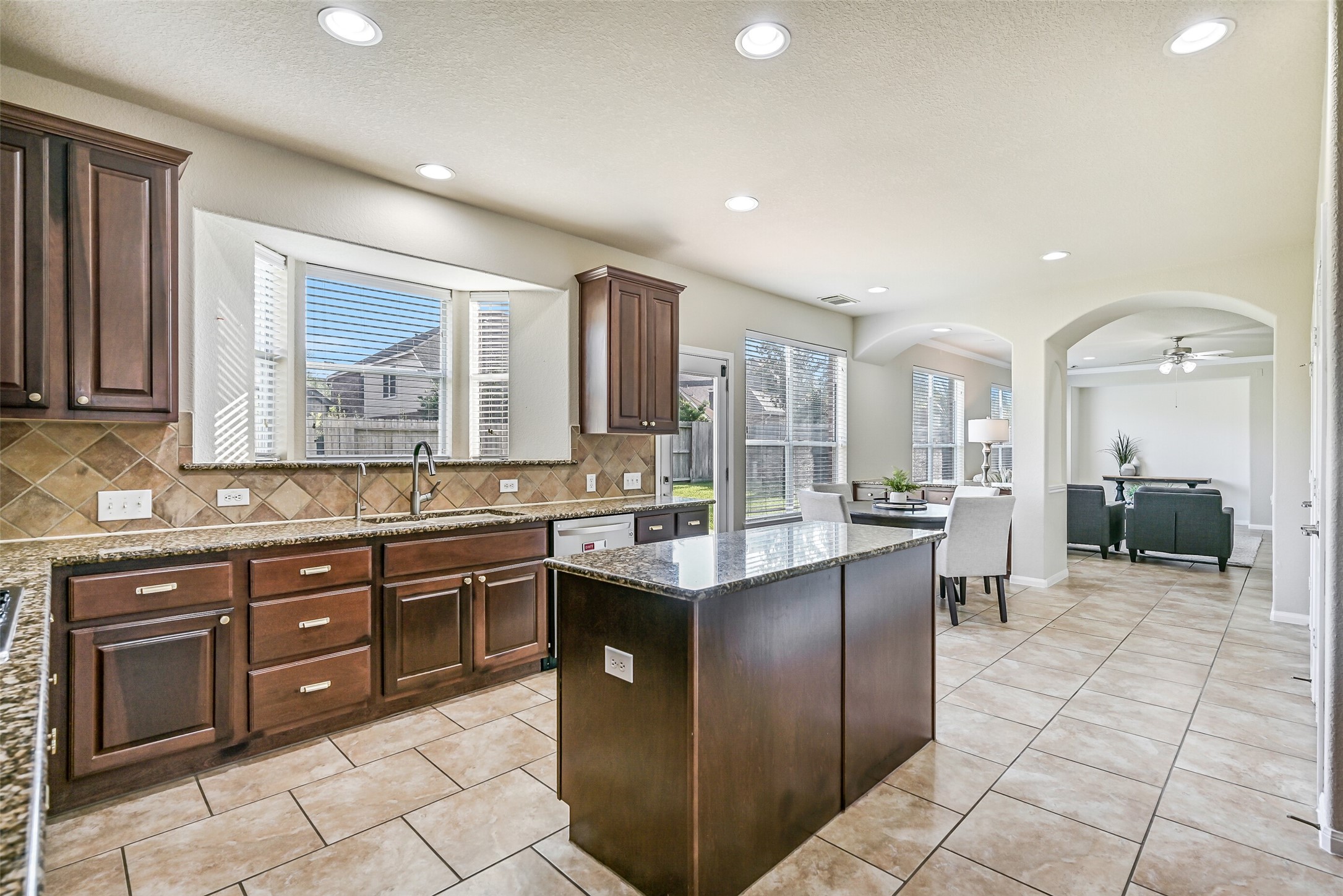 The large center island anchors the space and is complemented by a gas cooktop, built-in microwave, wall oven, and expansive granite surfaces. Recessed lighting and neutral finishes create a bright, welcoming environment that will easily become the hub of daily life.