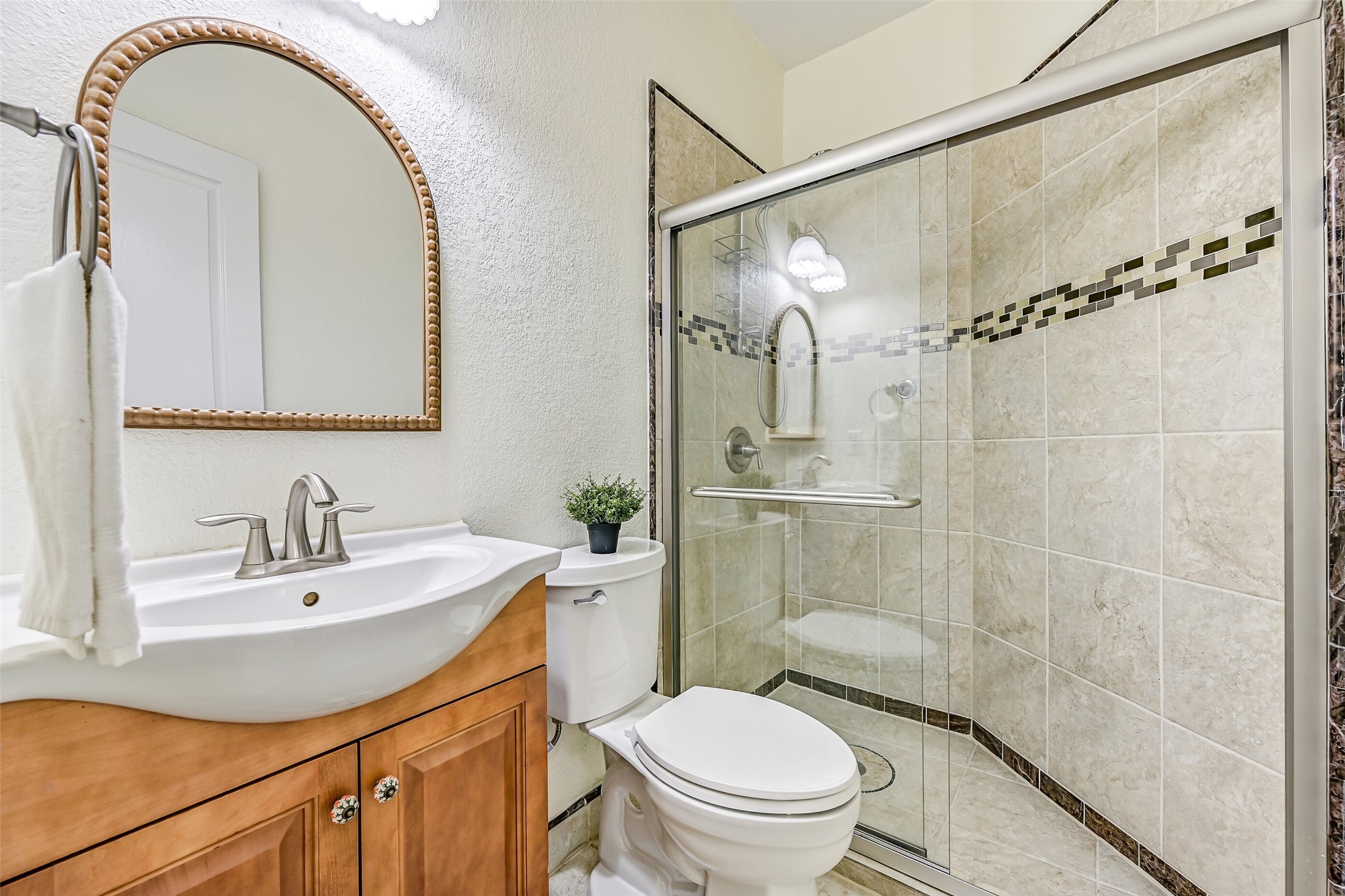 Conveniently located near the garage entrance and adjacent to the study, this full bathroom is ideal for both guests and everyday use. The space features tile flooring, a vessel sink atop a raised-panel vanity, a framed mirror, and a walk-in shower with a sliding glass enclosure, decorative accent tile, and a full tile surround.