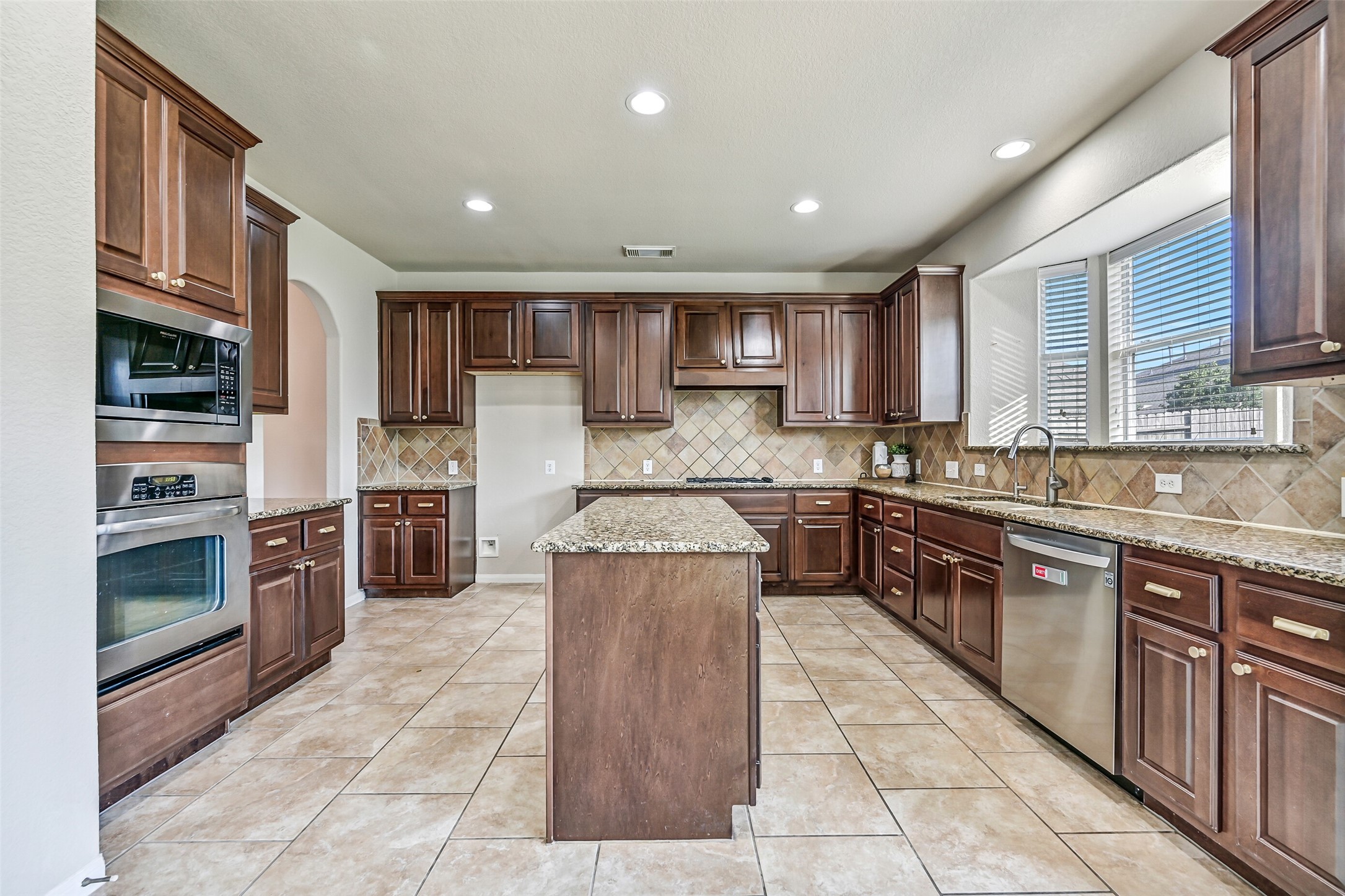 Continue into the heart of the home where this impressively sized island kitchen showcases gleaming granite countertops, a diagonally laid tile backsplash, recessed lighting, and an abundance of richly stained raised-panel cabinetry. The oversized center island provides additional prep space, storage, and a natural gathering spot for family and friends.