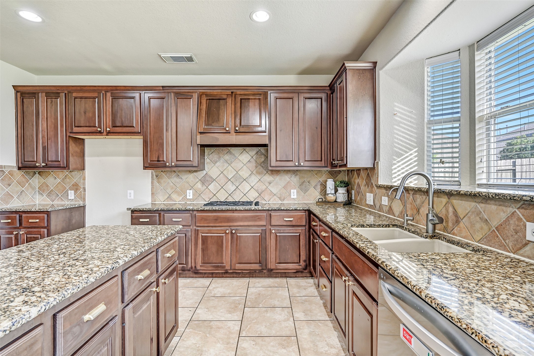 Designed with both functionality and style in mind, the kitchen features granite counters that stretch for days, a dual-basin undermount sink beneath sunny backyard-facing windows, stainless dishwasher, and ample workspace for preparing everything from weeknight dinners to holiday feasts.