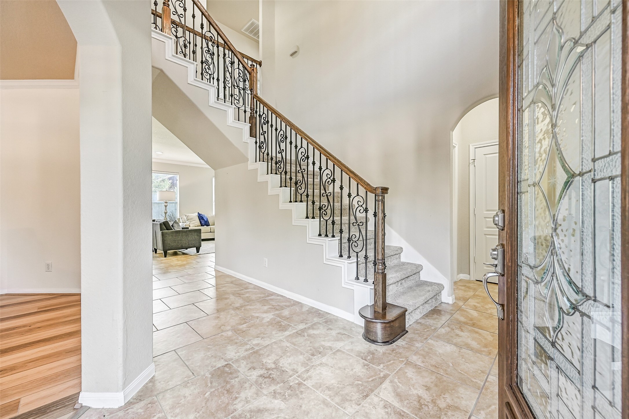 Step inside to a dramatic two-story foyer highlighted by fresh neutral paint, brick-laid ceramic tile flooring, and an elegant split staircase with decorative wrought iron balusters and plush new carpet. Natural light pours through the leaded glass front door, creating a bright and welcoming first impression.