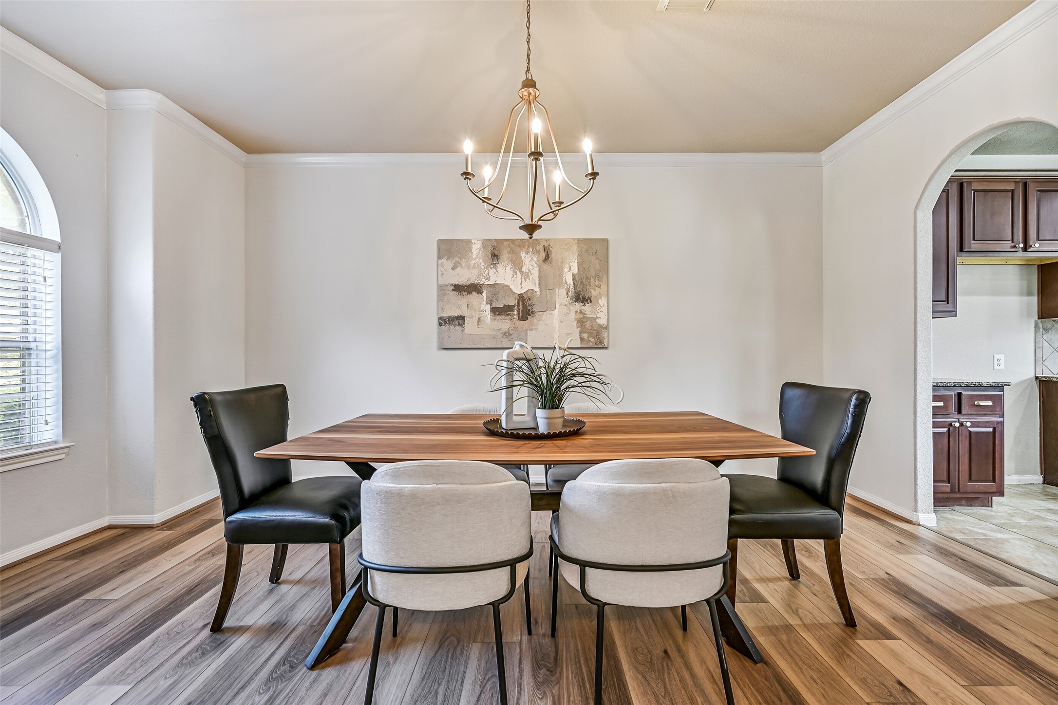 Continue through a second arched opening into the stately formal dining room, where crown molding, fresh paint, and luxury vinyl plank flooring create an elegant backdrop for holiday gatherings and special occasions. A brushed nickel five-light chandelier anchors the space overhead, while direct access to the kitchen makes entertaining effortless.