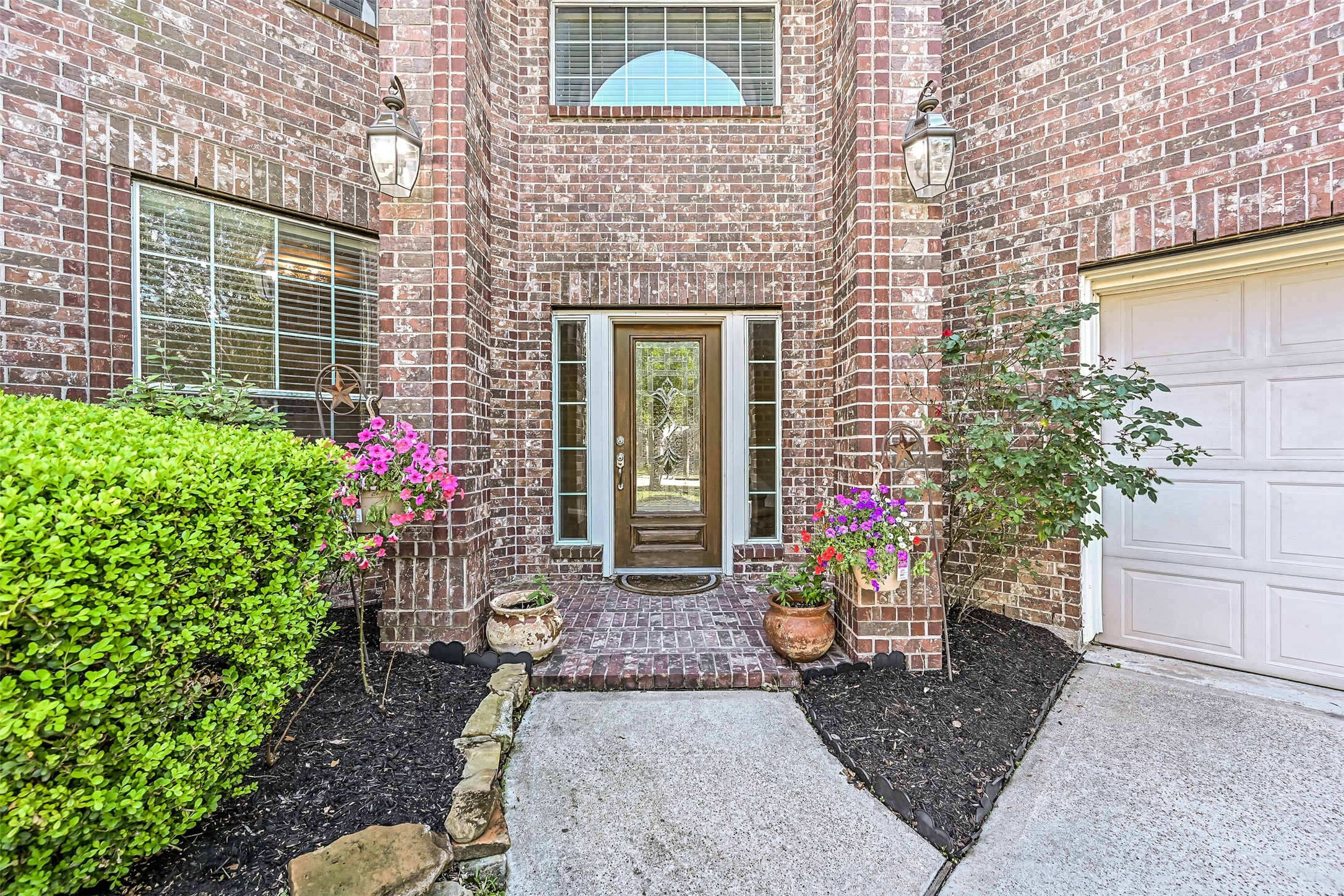 Follow the walkway to the diagonally positioned east-facing front door, tucked beneath a covered entry framed by towering brick columns. Decorative glass inserts, updated landscaping, and colorful seasonal blooms provide a welcoming introduction to the beautiful spaces that await inside.