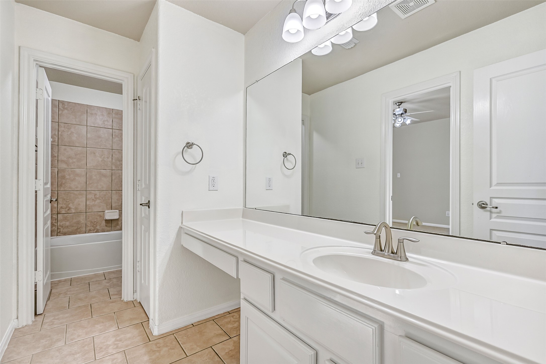 This Jack & Jill style bathroom serves the adjoining secondary bedrooms and is thoughtfully designed with separate vanity and bathing areas for added functionality. Features include a lengthy cultured marble countertop with an undermount basin sink, a seated makeup vanity with lap drawer, white cabinetry, updated lighting, tile floors, and a private combination bathtub and shower with a tile surround.