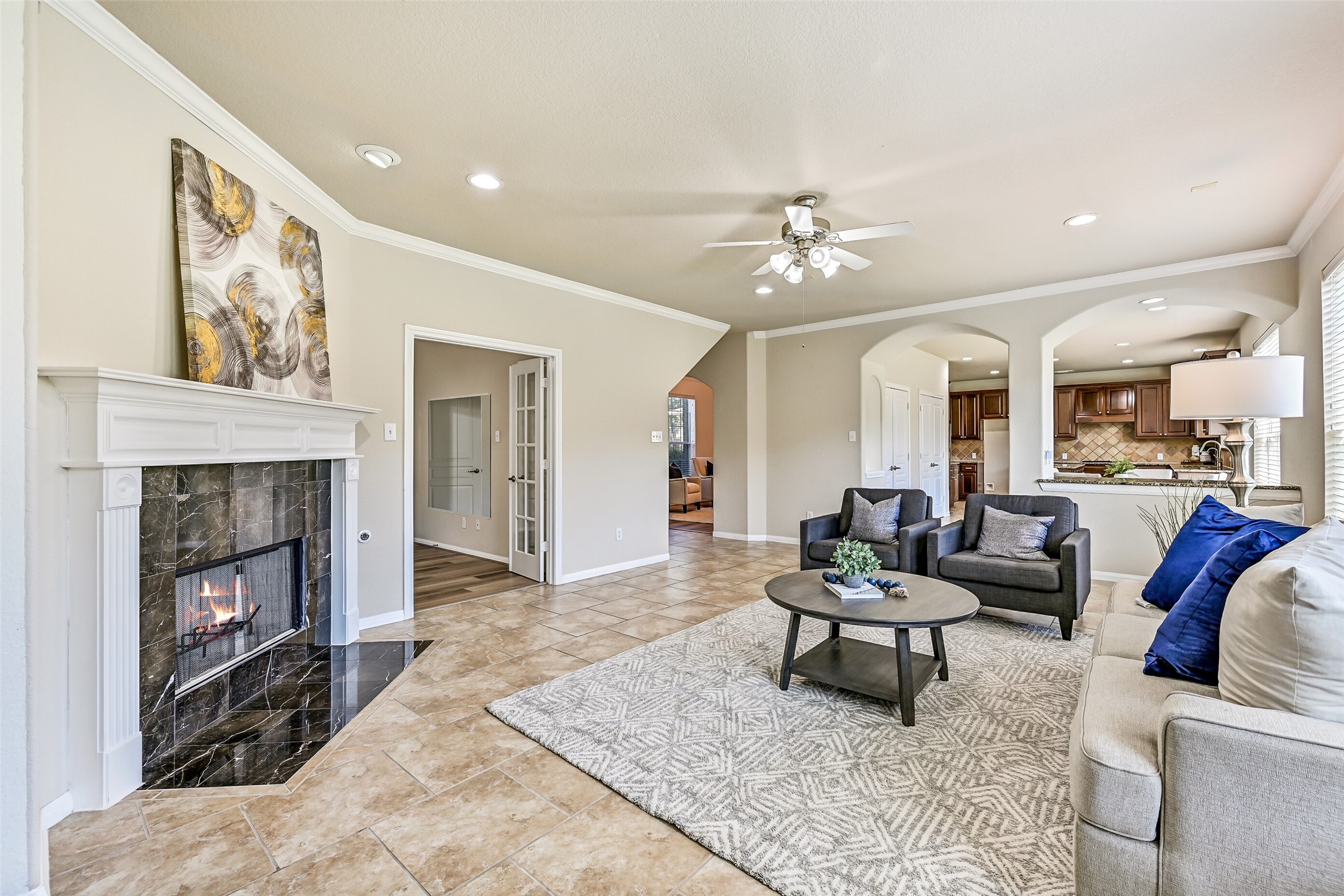 A corner-set gas log fireplace with a striking granite tile surround and classic white mantle anchors the family room and creates a natural focal point for gatherings. From this vantage point, notice the open connection to the kitchen, breakfast room, and adjacent study, enhancing the home's functional flow.