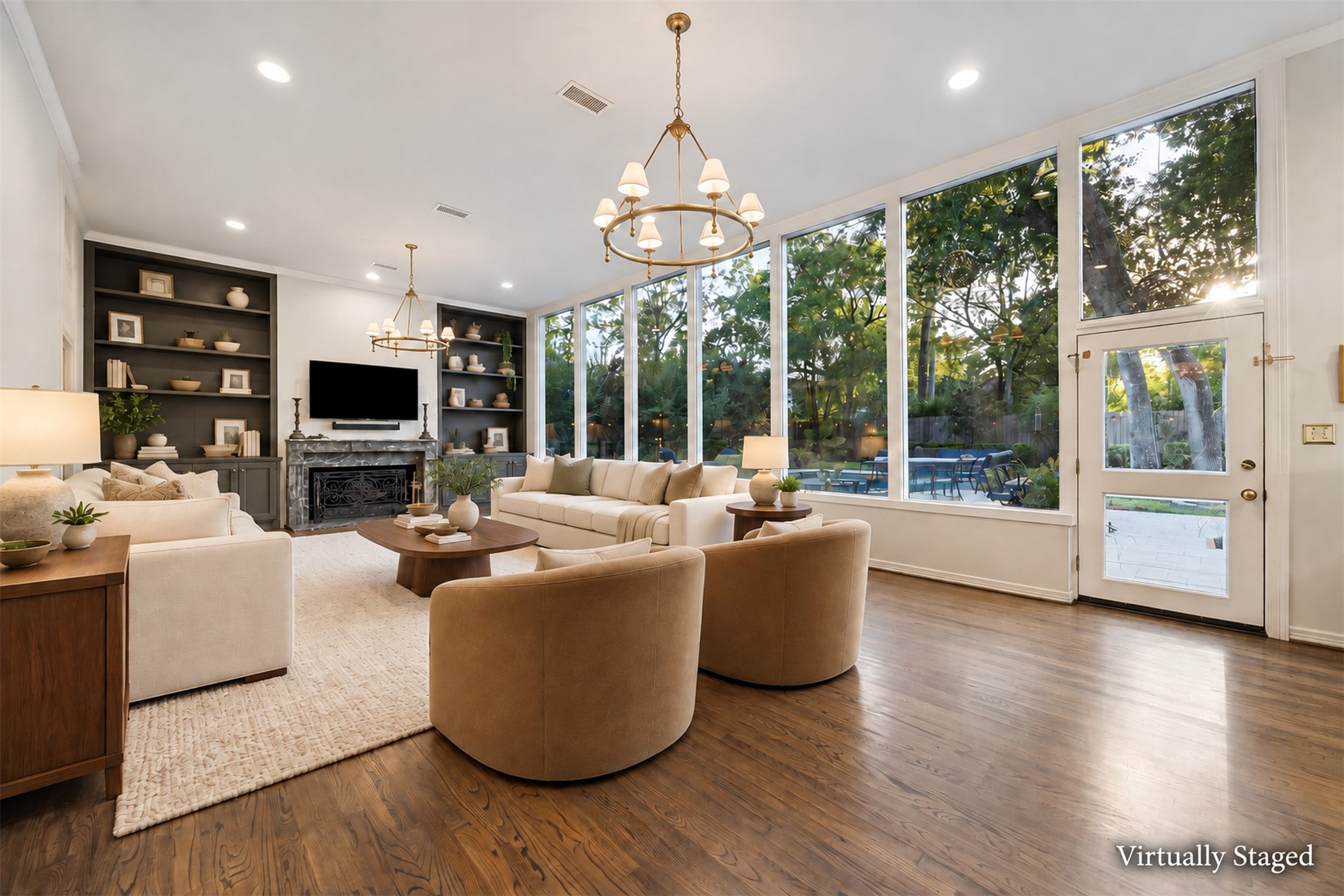 Virtually Staged - Expansive living room with wall of windows offering stunning views of the maturely landscaped backyard complemented by elegant built-in shelving and an oversized fireplace, perfect for relaxing or entertaining.