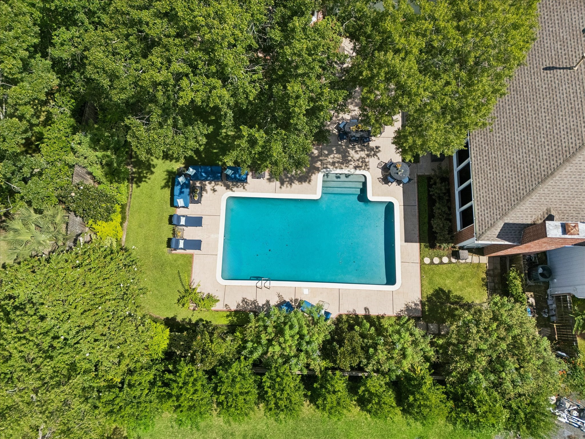 Aerial view of a spacious backyard oasis featuring a large, inviting swimming pool surrounded by lush greenery and ample patio space for relaxation and entertaining.