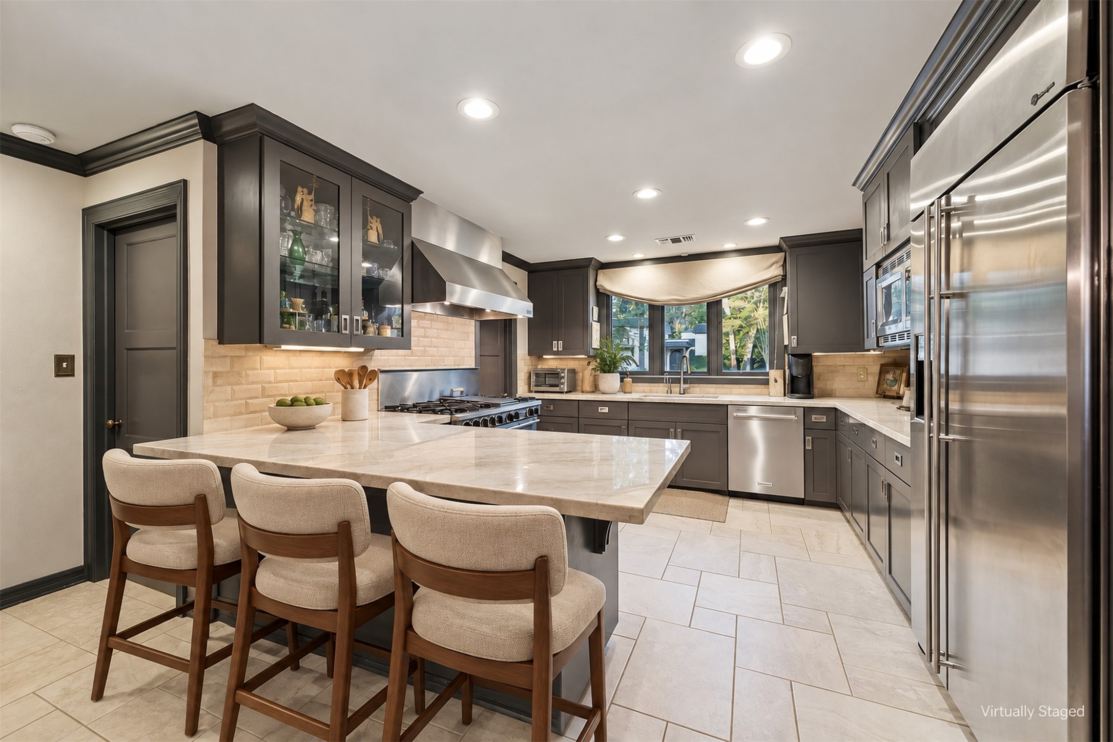 Virtually Staged - Modern kitchen with sleek stainless steel appliances, elegant marble countertops, and ample cabinetry. The layout includes a breakfast bar and a view of the front yard.