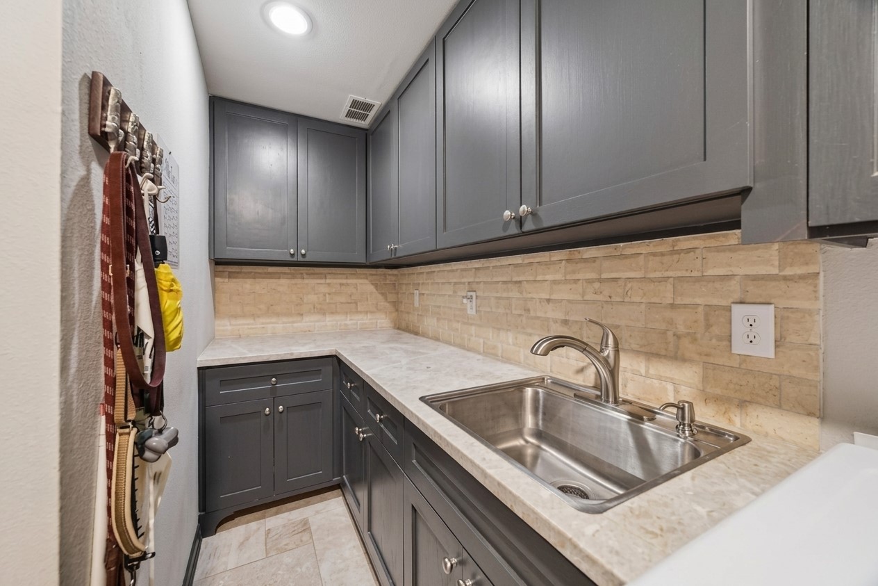 Effortlessly handle chores in this updated utility room, featuring ample storage with shaker cabinetry, a modern sink, and a stylish backsplash for ultimate functionality.