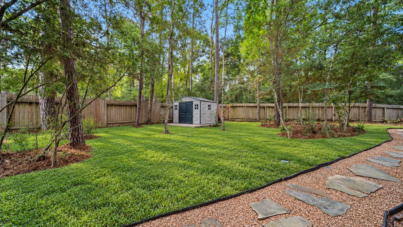 A little slice of nature right at home! This beautifully maintained backyard features mature shade trees, lush green grass, and a charming stepping-stone pathway. Shed included for landscaping equipment storage.