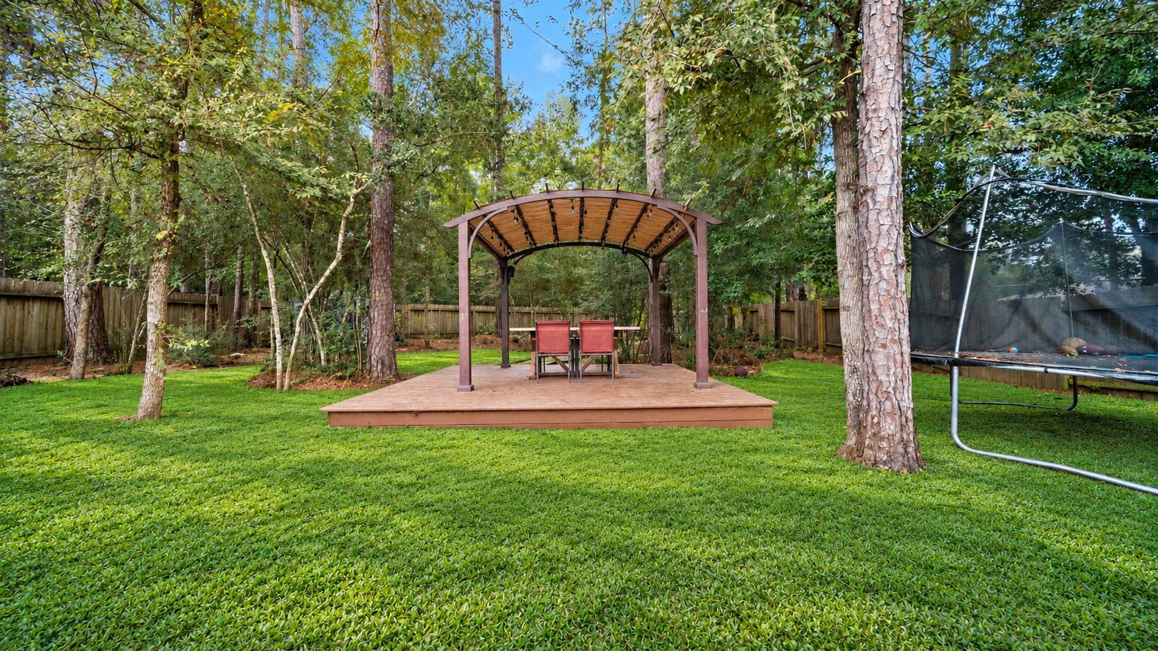 Imagine relaxing beneath the trees! This inviting backyard features a raised deck with a pergola, creating a wonderful space for outdoor dining or enjoying a peaceful evening. Outdoor furniture and trampoline not included.