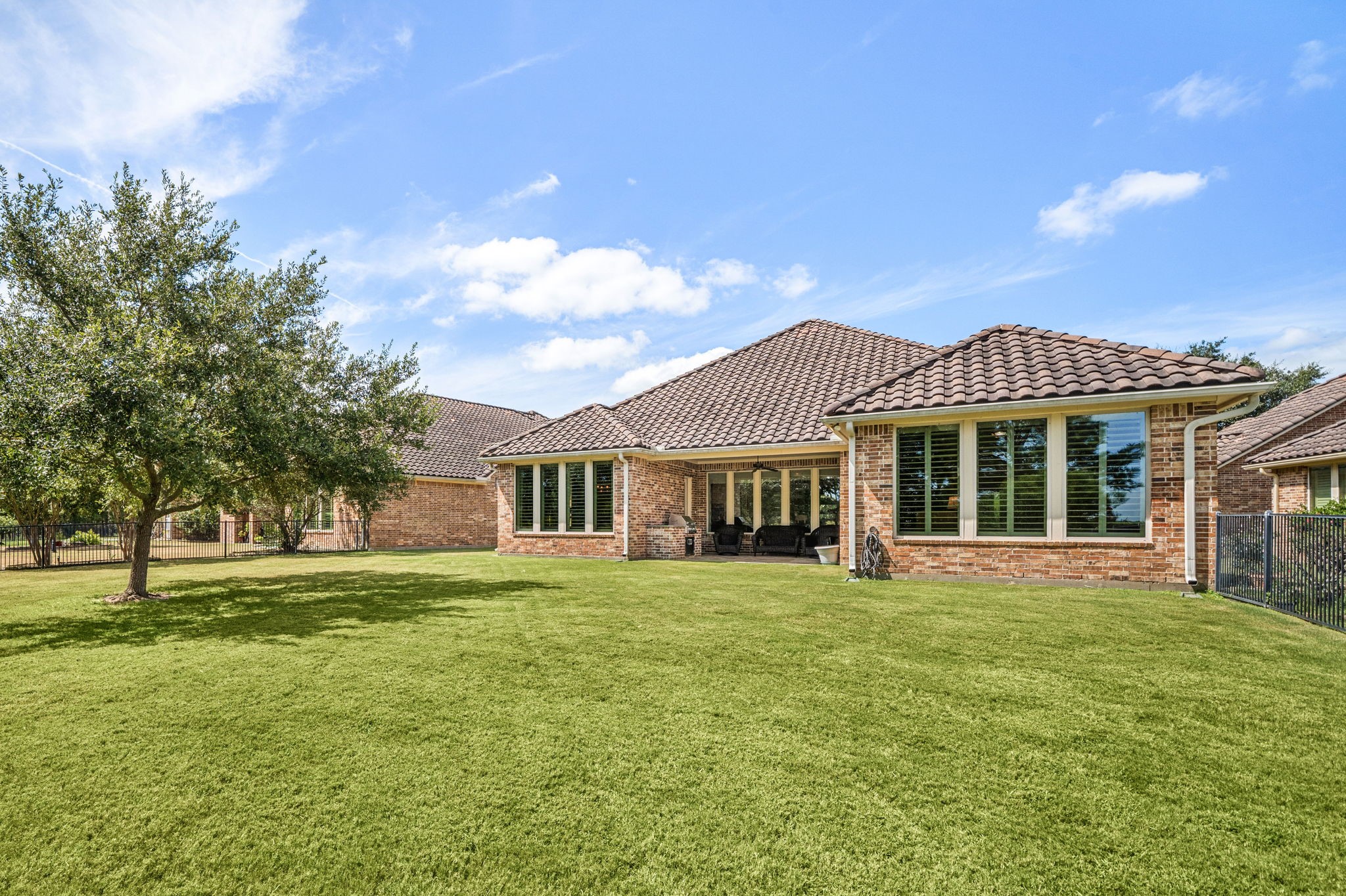 A sprawling backyard offers plenty of room to relax or entertain, shaded by mature trees and enclosed by a wrought iron fence.
