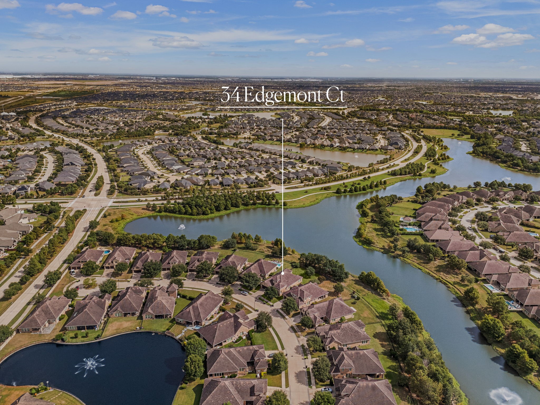 This aerial view highlights the home's prime setting along the community's scenic lake, with tree-lined streets and gated access throughout the neighborhood.