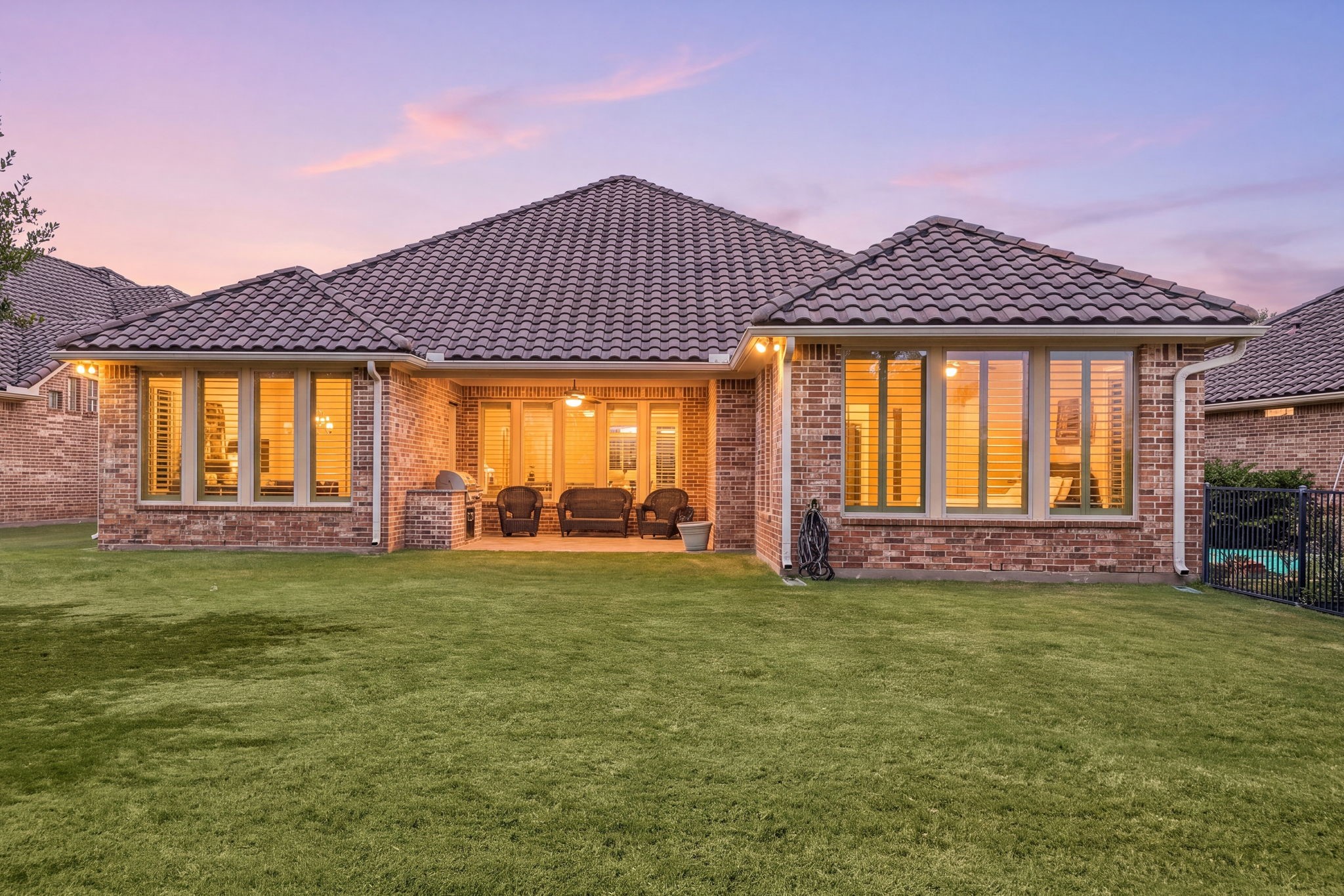 As evening falls, the home's warm lighting and covered patio create an inviting space to unwind outdoors.