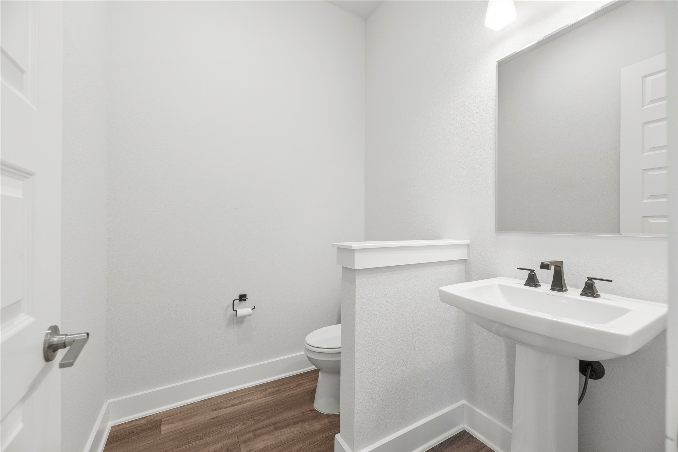 Convenient guest half bath complete with a classic pedestal sink, modern dark bronze fixtures, framed mirror, and privacy half-wall.