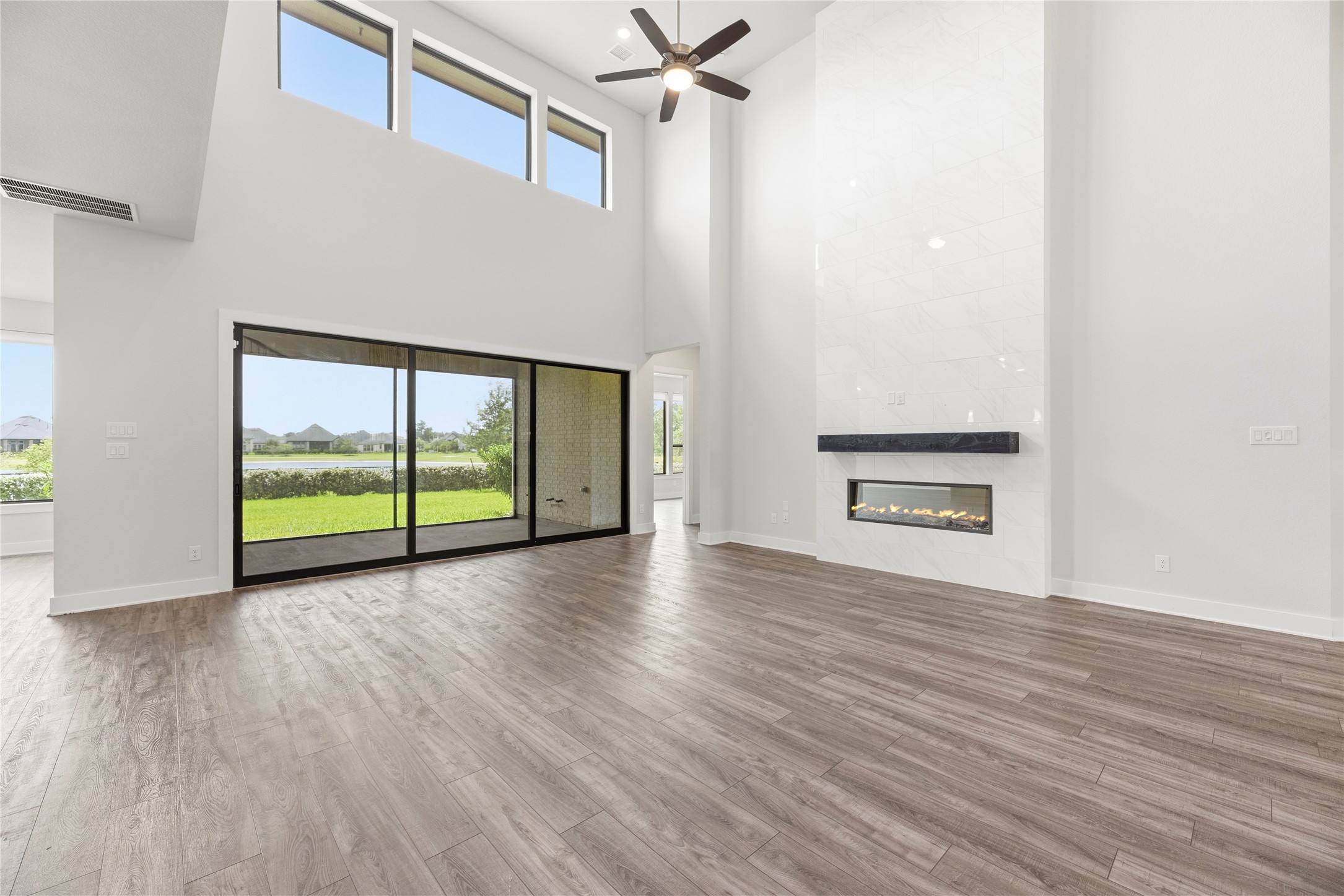 Focal point living room featuring a dramatic floor-to-ceiling tiled gas fireplace with mantel, two-story upper transoms, and sliding glass doors leading to the covered back porch.
