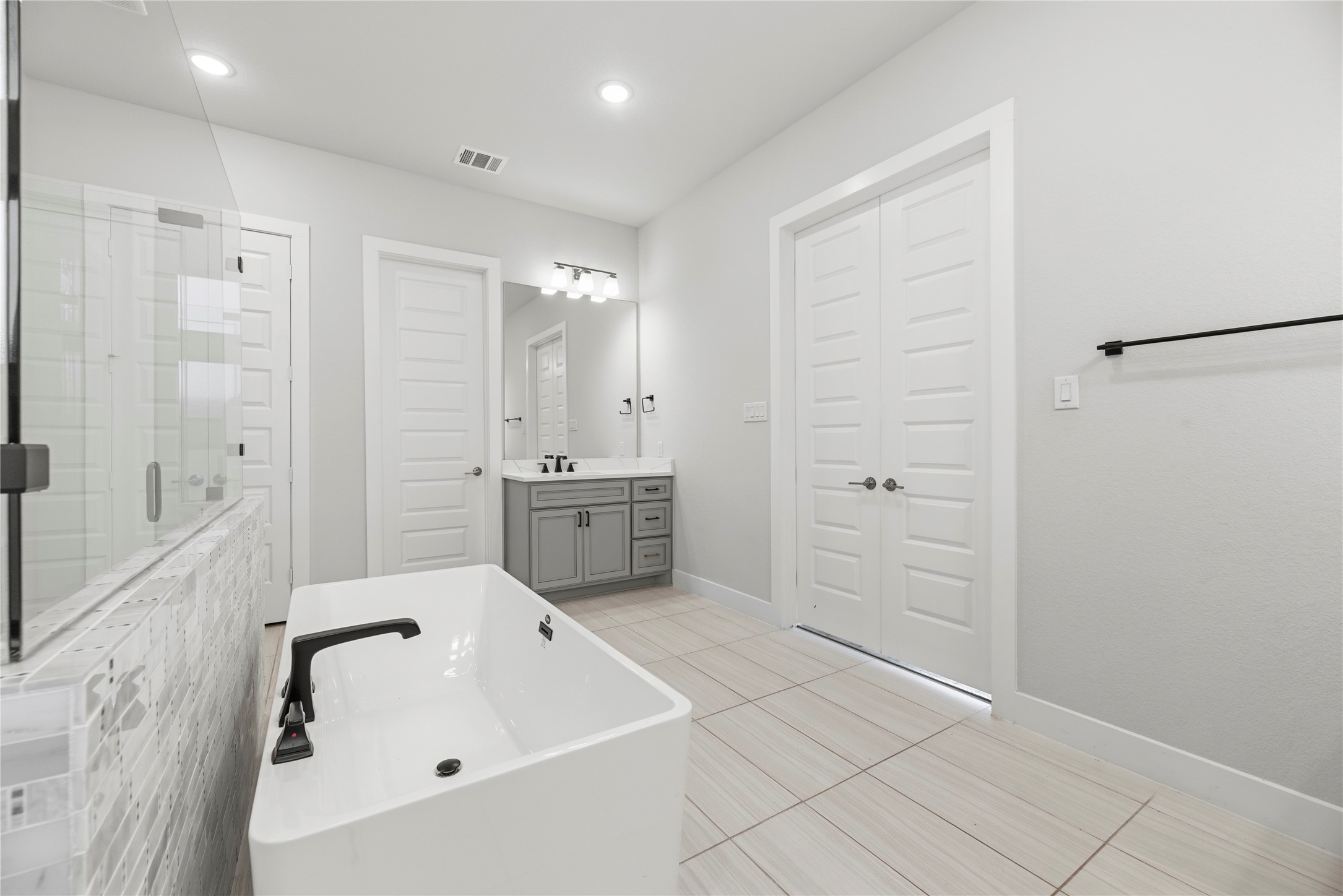 Spacious layout overview showing double-door bedroom entry, grey shaker cabinetry with quartz countertops, matte black hardware, and bright recessed lighting.