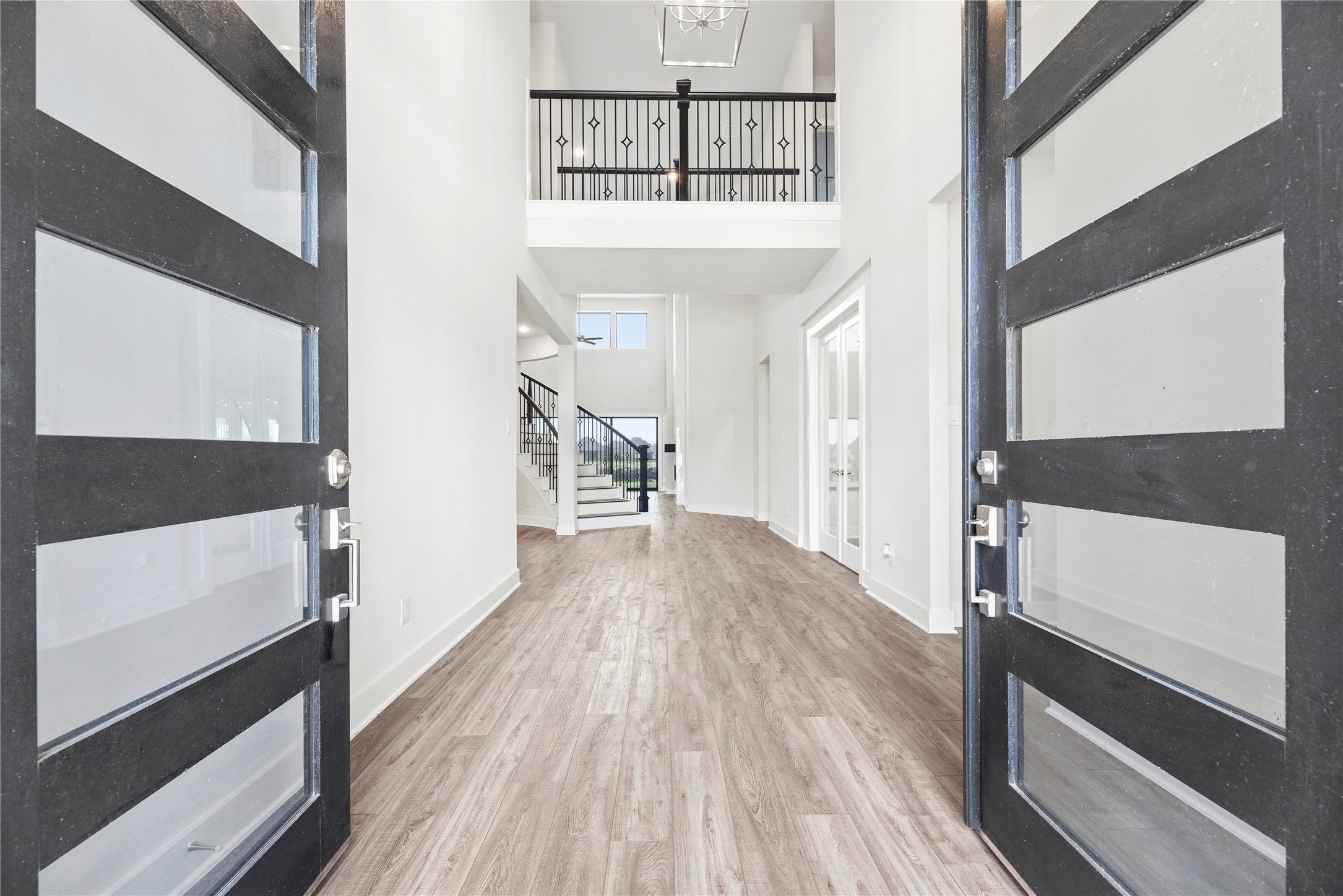 Grand entrance showcasing glass-panel double doors, soaring two-story ceilings, open iron-railed overlook, and a clear line of sight to the back living space.