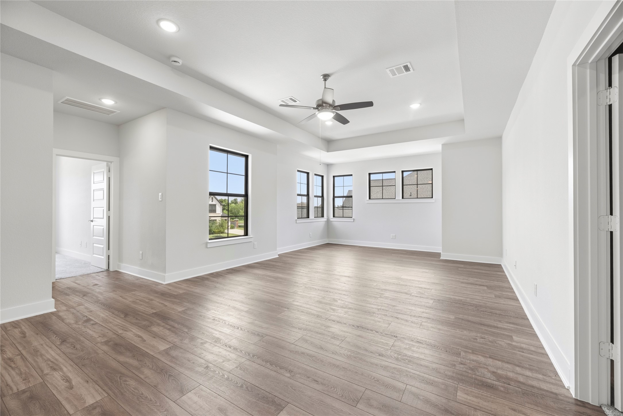 Generous game room featuring tray ceilings, wood-look flooring, and custom built-in white shelving along the rear wall.