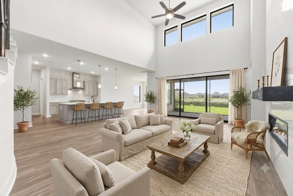 Breathtaking open-concept living area featuring soaring two-story ceilings, wall of glass sliding doors to the patio, modern tile fireplace, and direct flow to the gourmet kitchen.