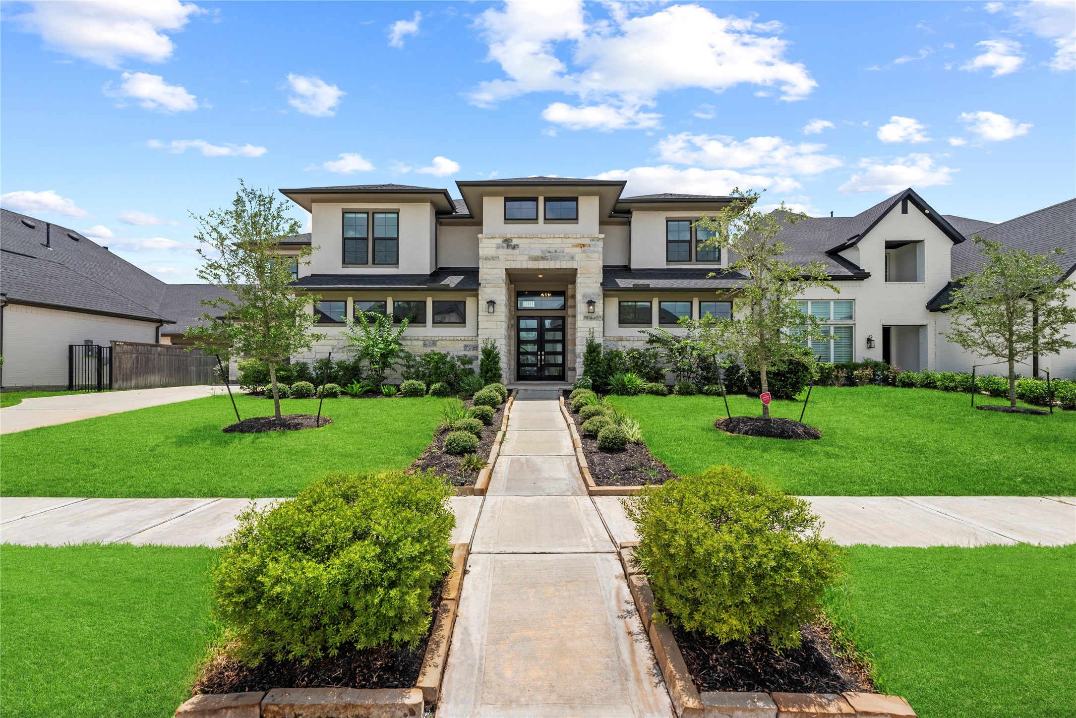 Impressive curb appeal featuring modern double front doors, stone accent pillar entrance, and pristine professional landscaping under clear blue skies.