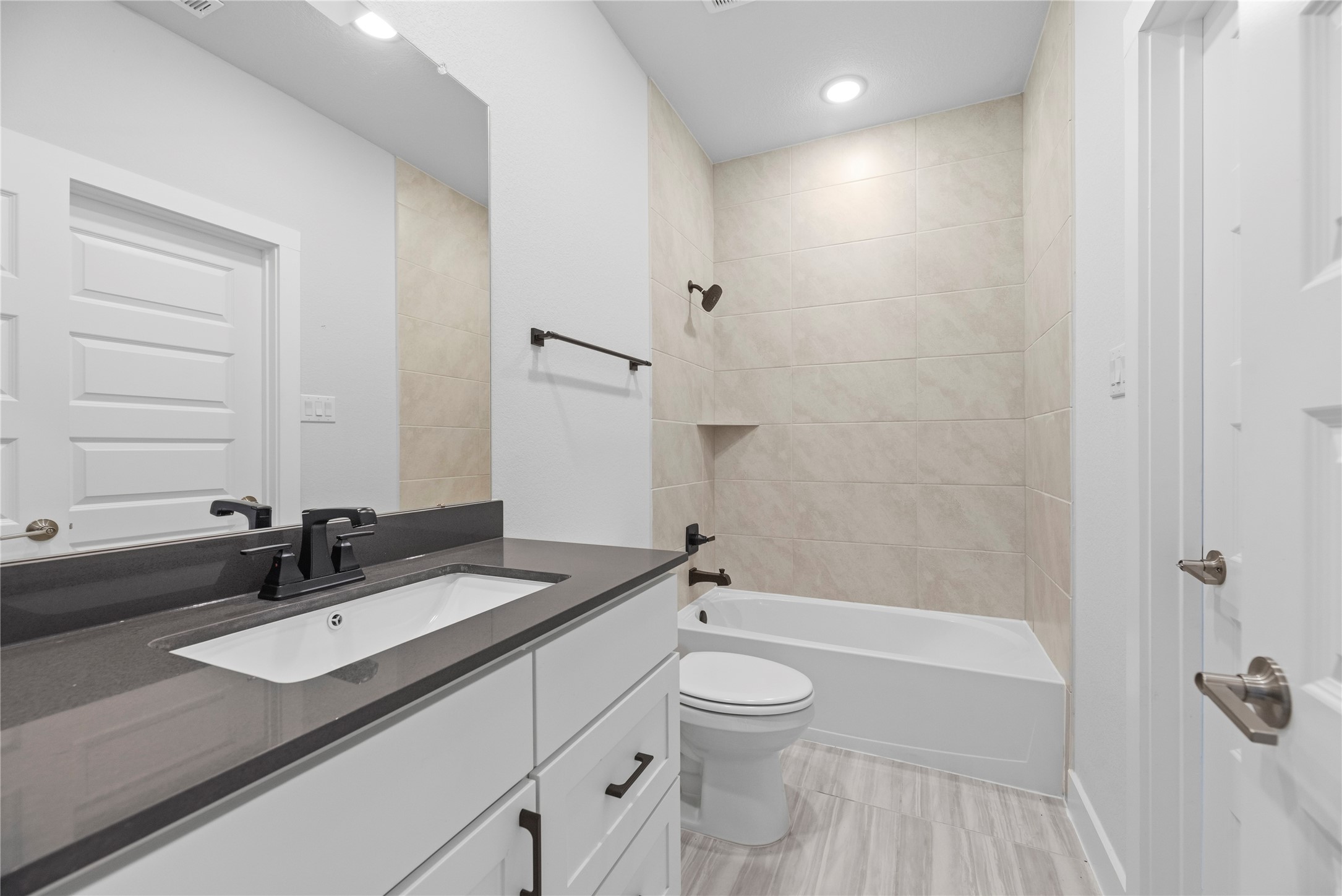 Well-appointed bathroom equipped with a dark quartz vanity, white cabinetry, matte black hardware, and a tiled tub/shower combination.