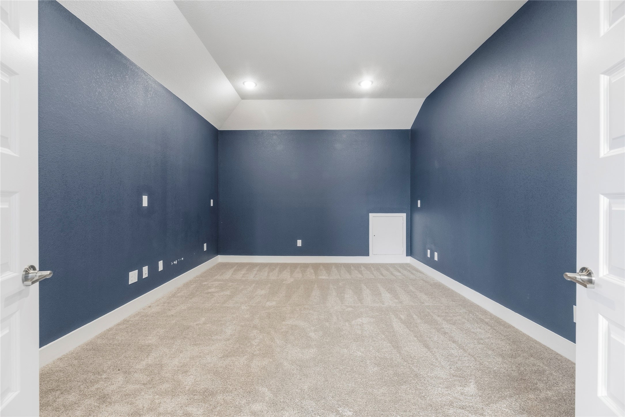 Enter through double doors into a private media room featuring rich navy accent walls, plush carpeting, recessed lighting, and built-in access storageideal for movie nights.