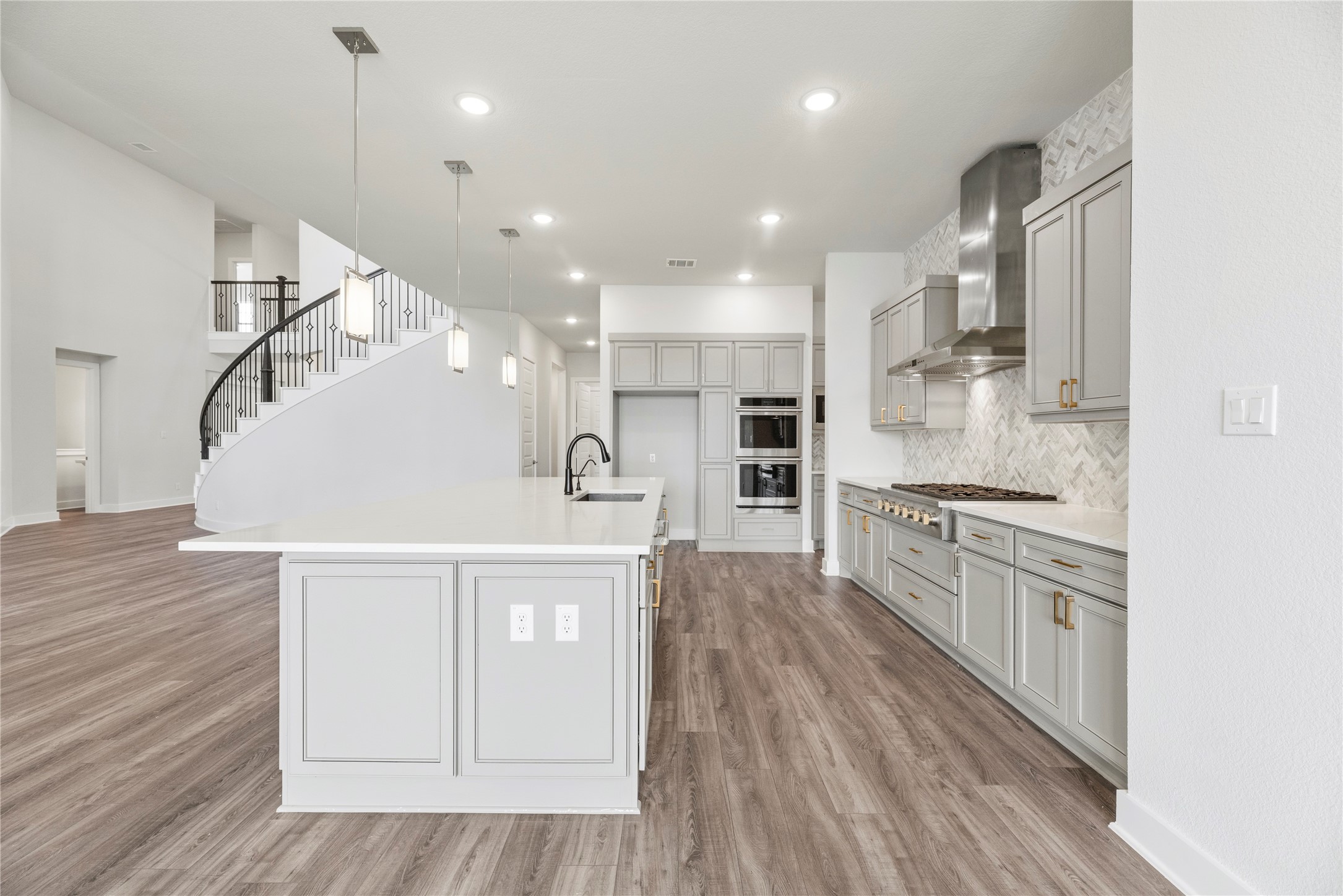 Angle showcasing the clean sightlines, abundant drawer and cabinet storage, gold/brass pull accents, built-in double ovens, and nearby grand foyer view.