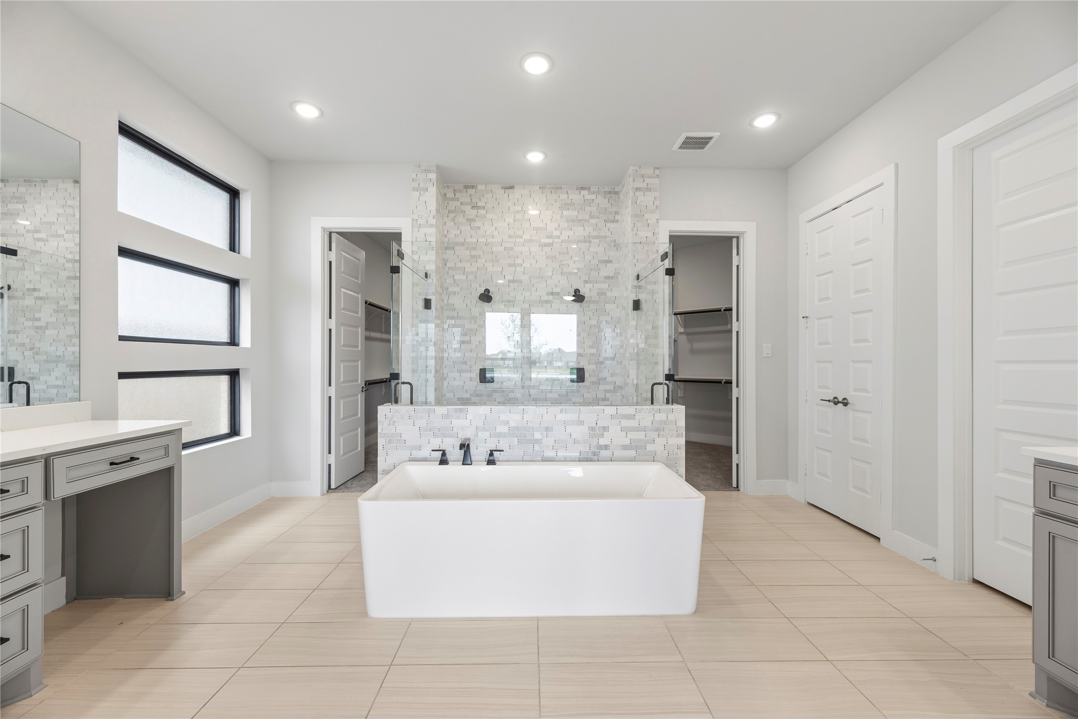 Luxurious primary bath showcase featuring a modern freestanding soaking tub, mosaic tile feature wall, walk-in shower with dual heads, split dual vanities, and dual walk-in closets.