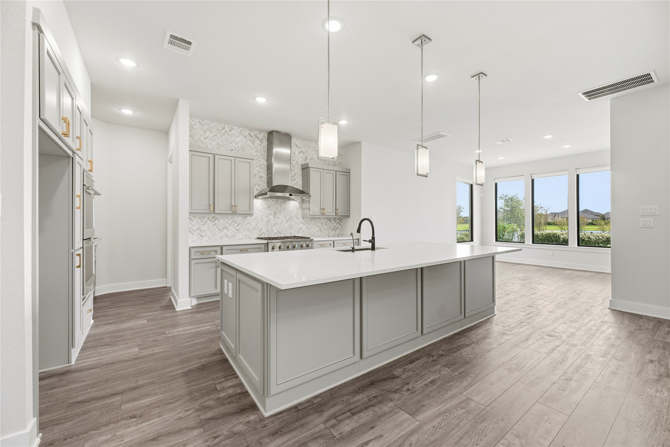 Modern chef's kitchen featuring soft-grey shaker cabinetry, quartz countertops, a large seating island, modern pendant lighting, and herringbone tile backsplash.
