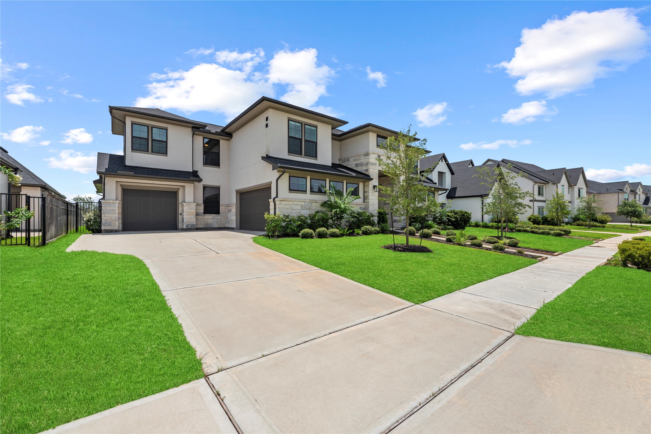 Wide side angle showing off the expansive concrete driveway, multi-car garage space, stone and stucco exterior, and charming neighborhood streetscape.