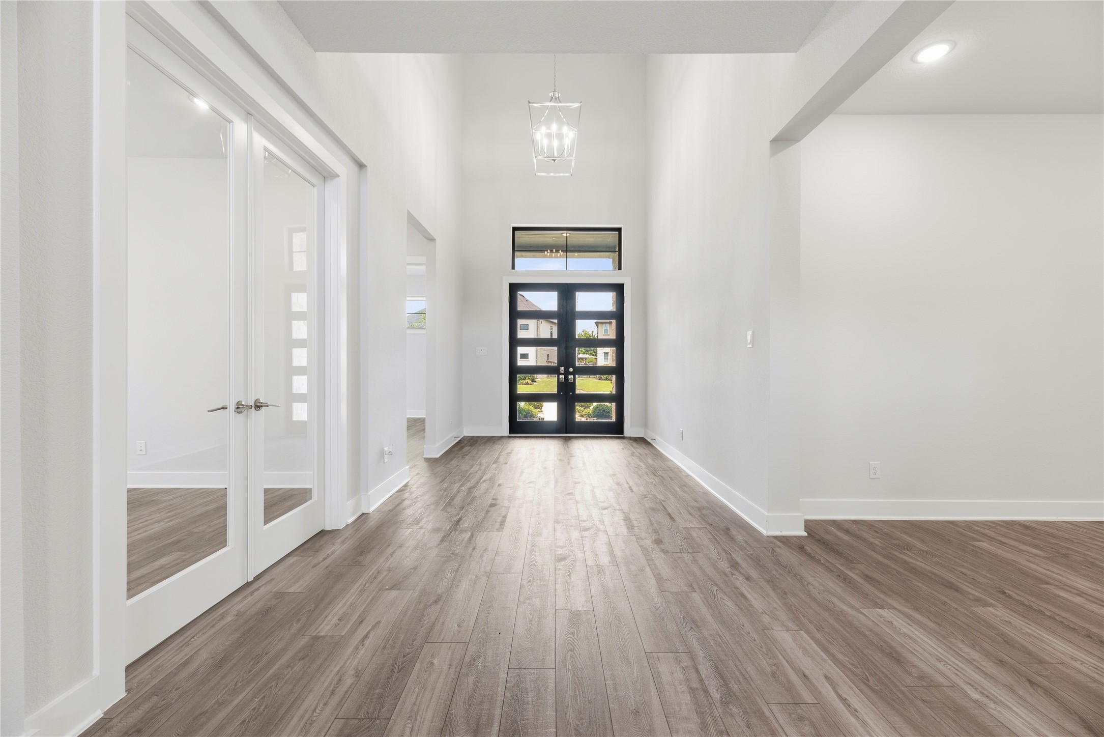 Wide, light-filled foyer featuring double glass front doors, high ceilings with a classic statement pendant light, and French-door entry into the private study.
