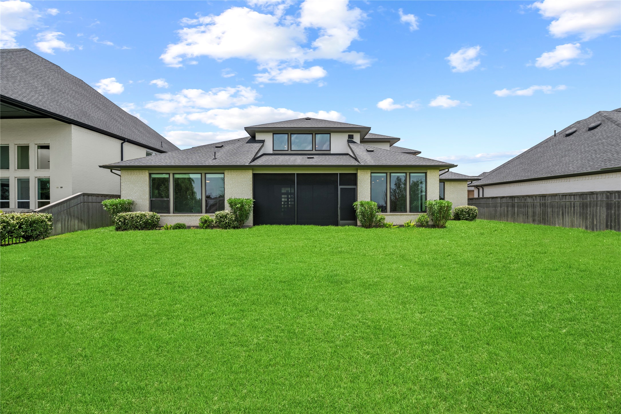 Direct back view showcasing the home's contemporary rooflines, brick and stucco finishes, screened patio, and flat, lush lawn.