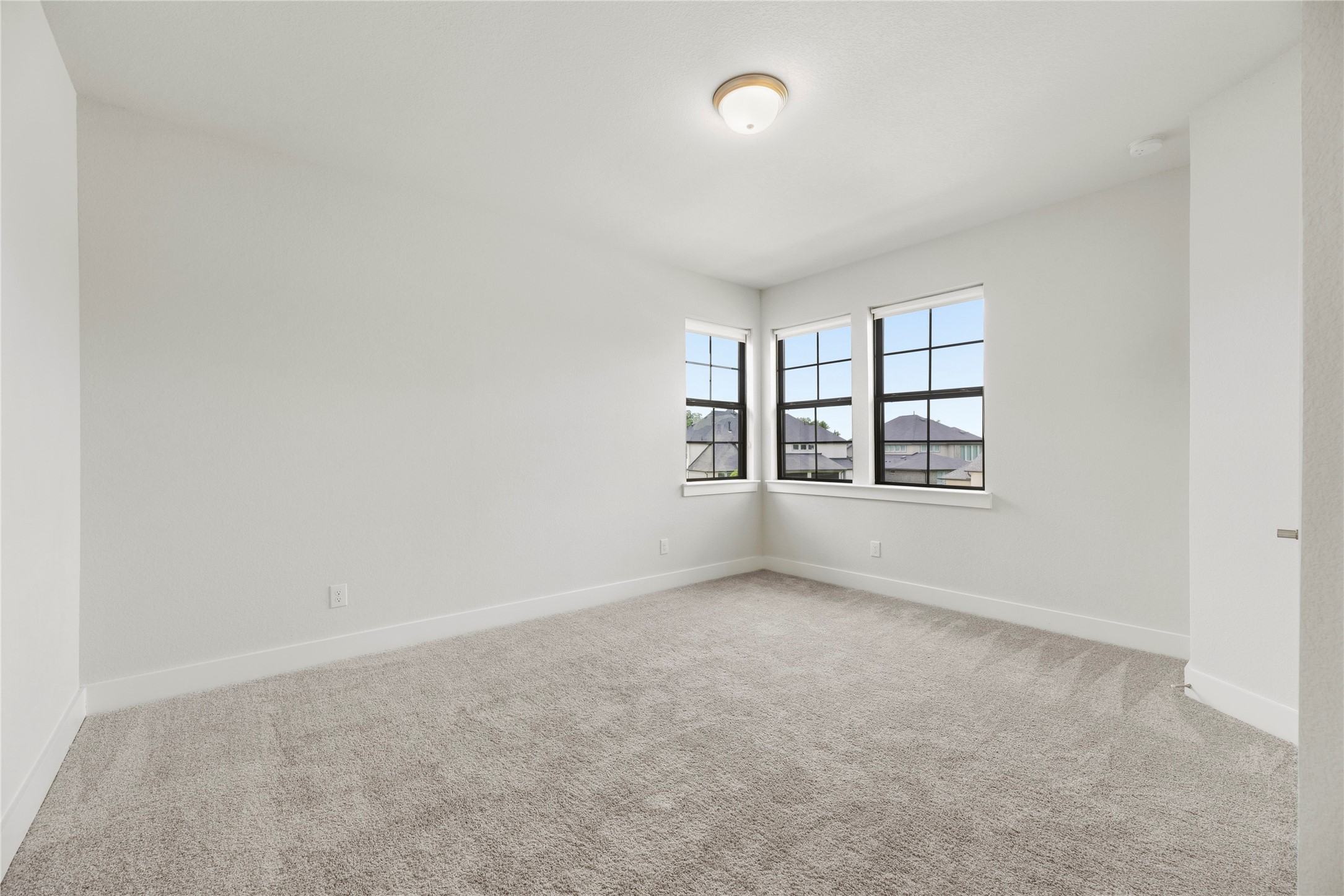 Light-filled guest room featuring cozy plush carpeting, clean white trim, and corner windows bringing in abundant natural light.