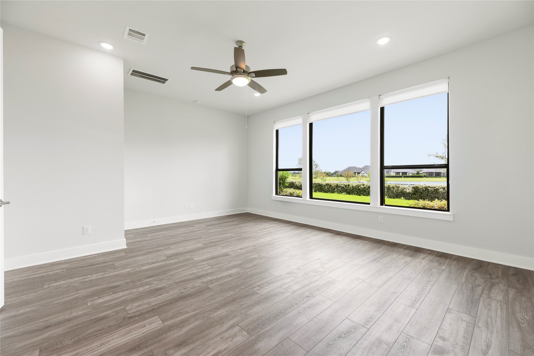 Bright and spacious primary bedroom featuring wall-to-wall wood-look flooring, ceiling fan, and large picture windows framing serene lake views.