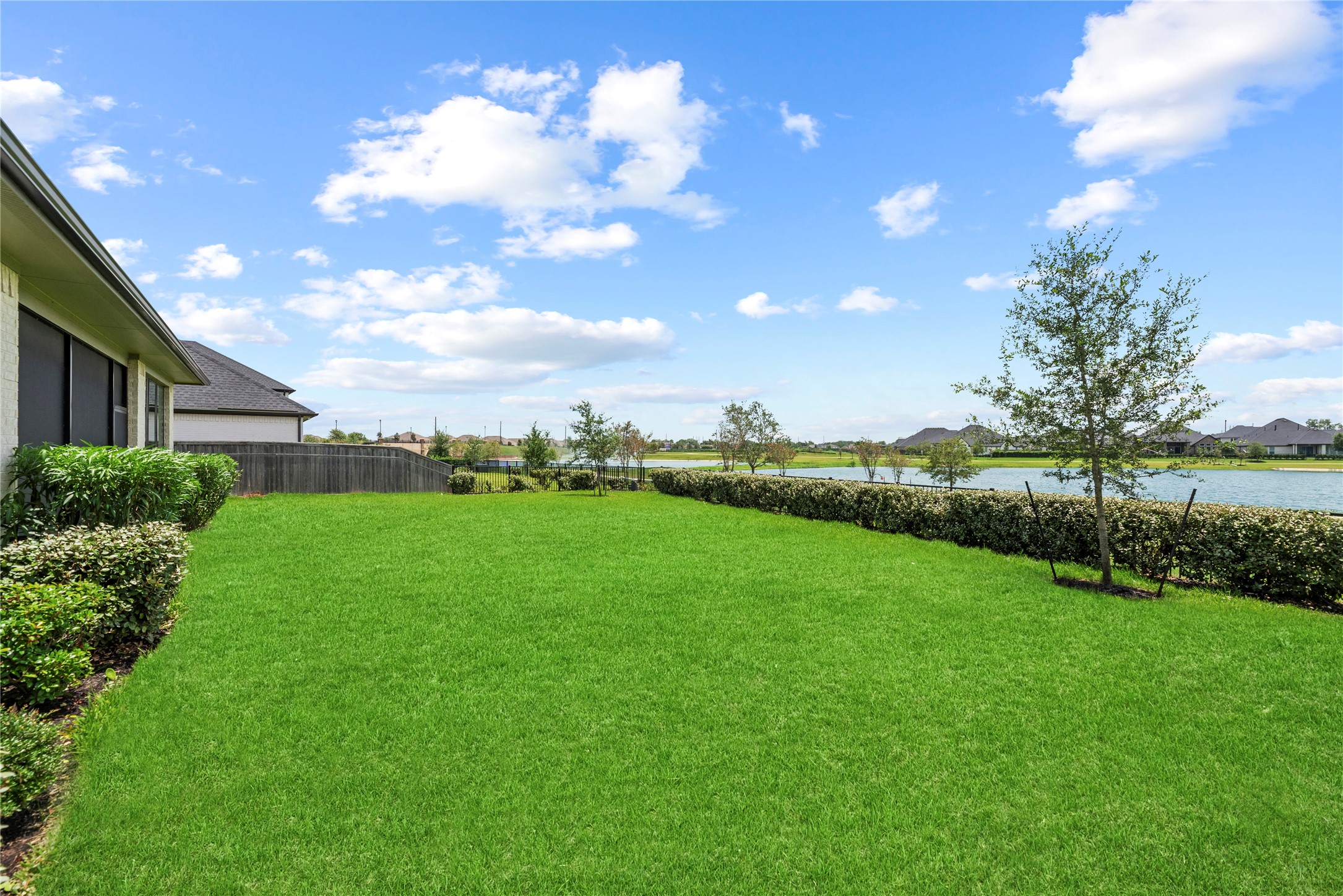 Generous green yard bordered by tailored hedges with direct views out over the neighborhood lake and community green space.