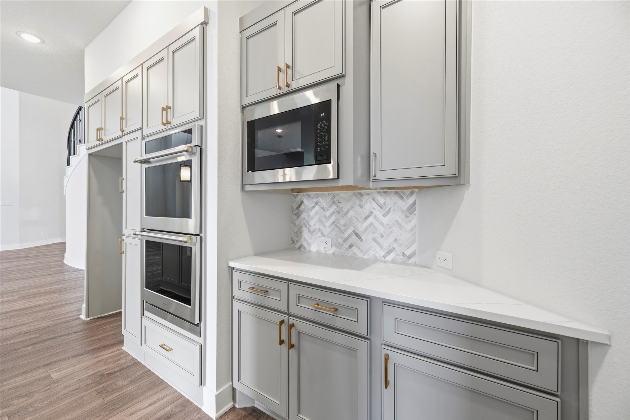 Built-in wall feature complete with double wall ovens, separate built-in microwave, beverage/prep counter with matching herringbone backsplash, and upper storage cabinets.