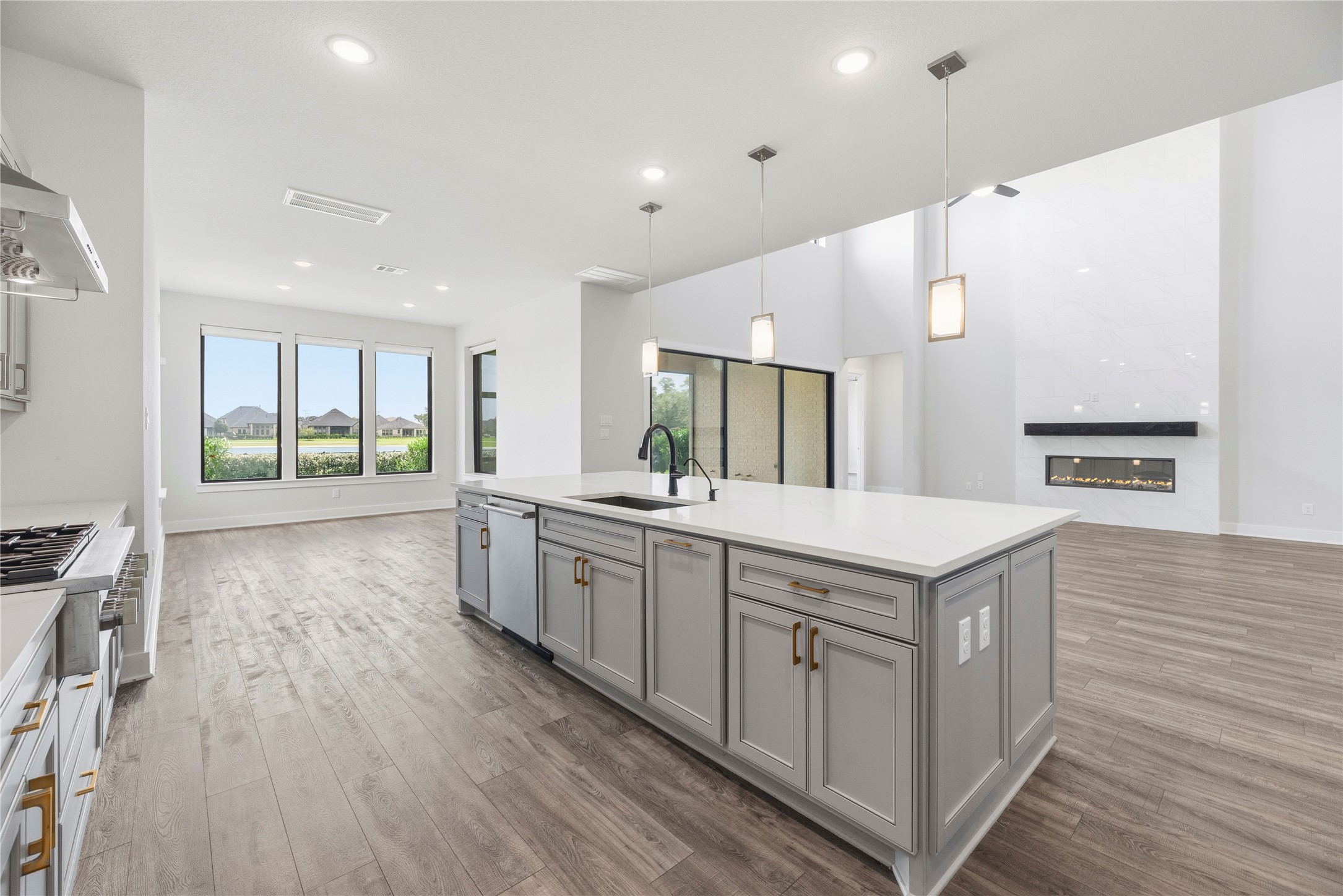 Functional view from behind the kitchen island featuring an undermount stainless steel sink, built-in dishwasher, and direct sightlines to the fireplace and water-view windows.