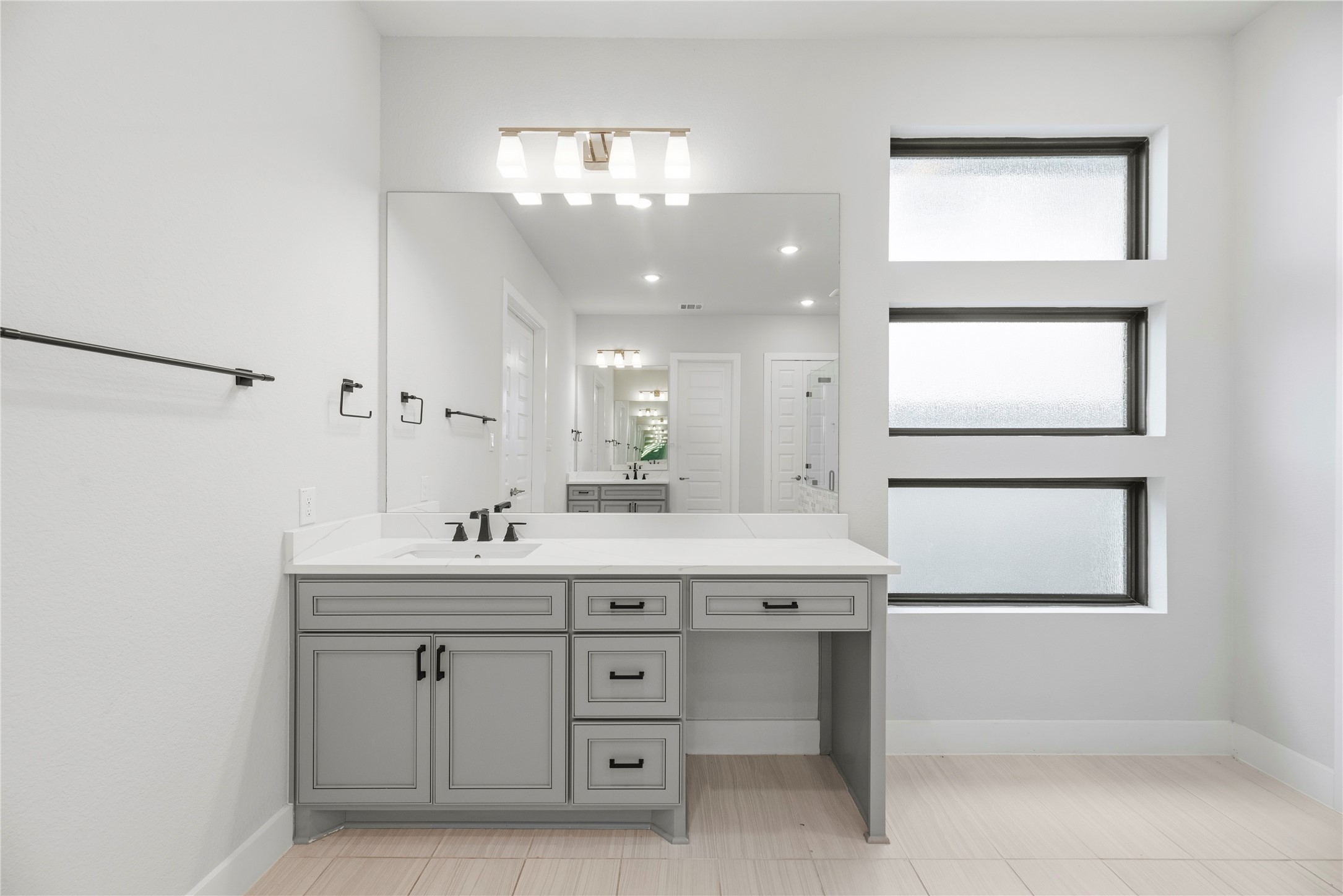 Custom grey vanity unit equipped with quartz countertop, under-mount sink, integrated seated makeup vanity area, and contemporary bath lighting.