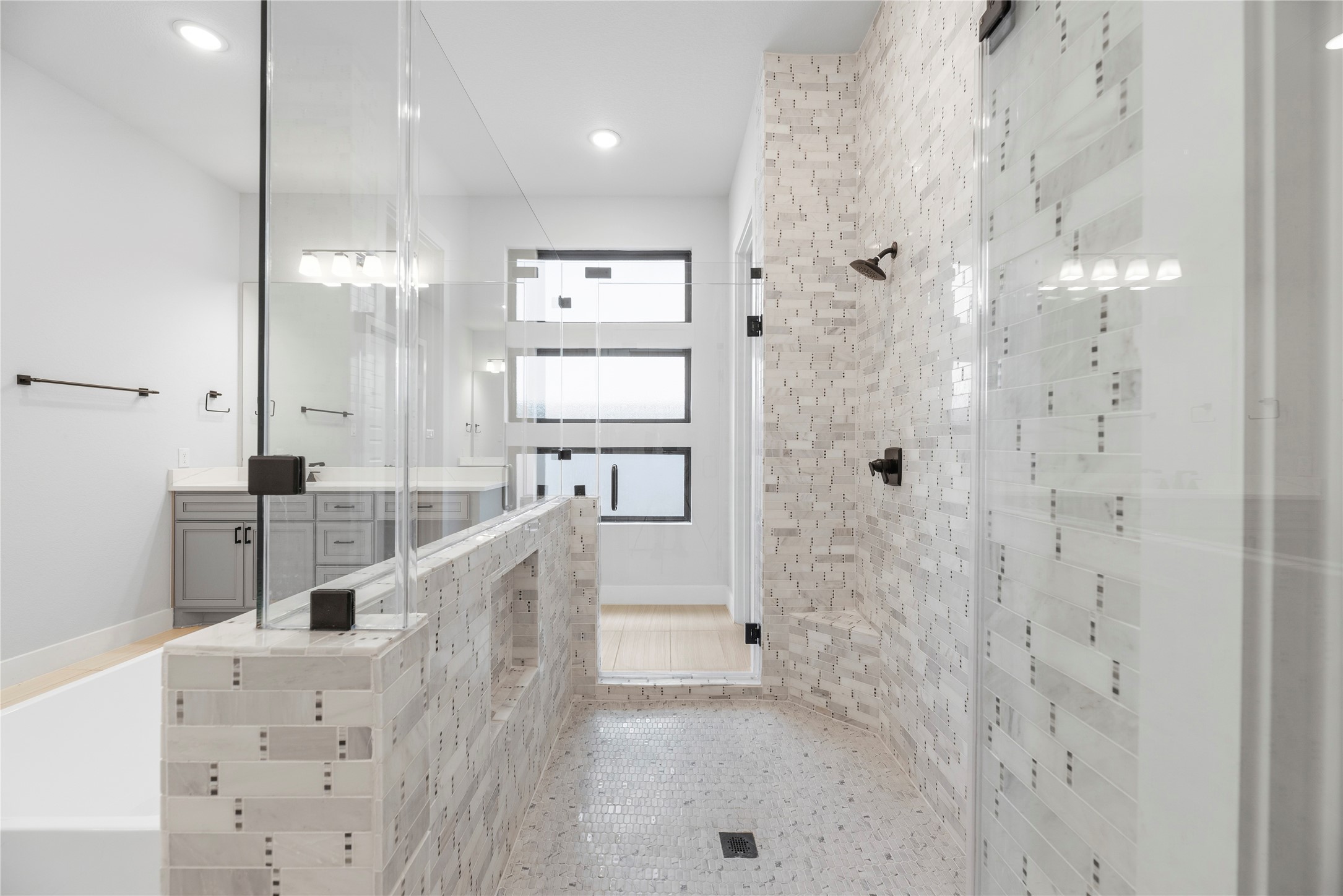 Deluxe tiled walk-in shower complete with dual shower heads, mosaic tile detailing, built-in seating bench, and sleek frameless glass enclosure.