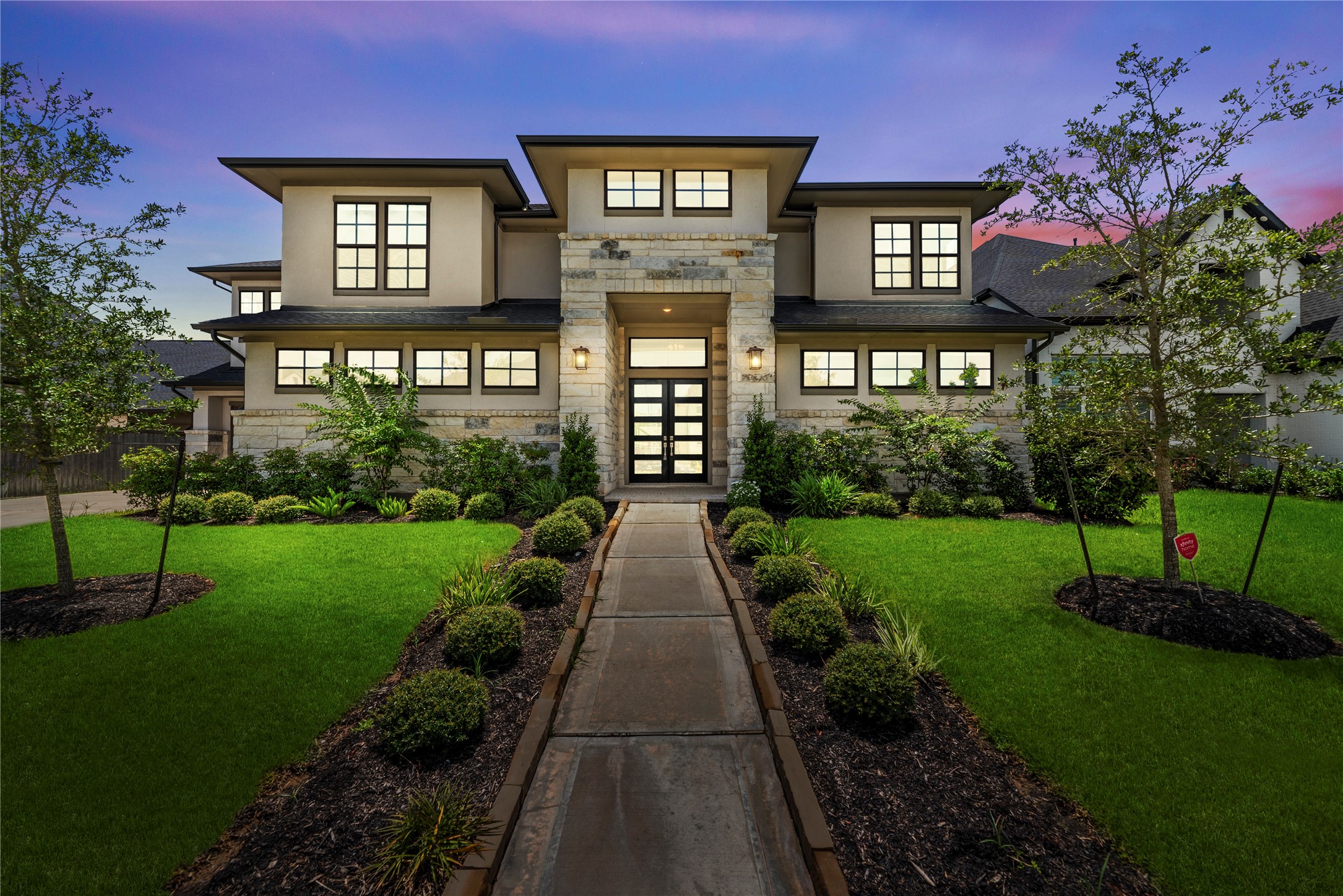 Striking twilight photo highlighting the homes grand stone entrance, contemporary geometric architecture, accent lighting, and manicured walkways.