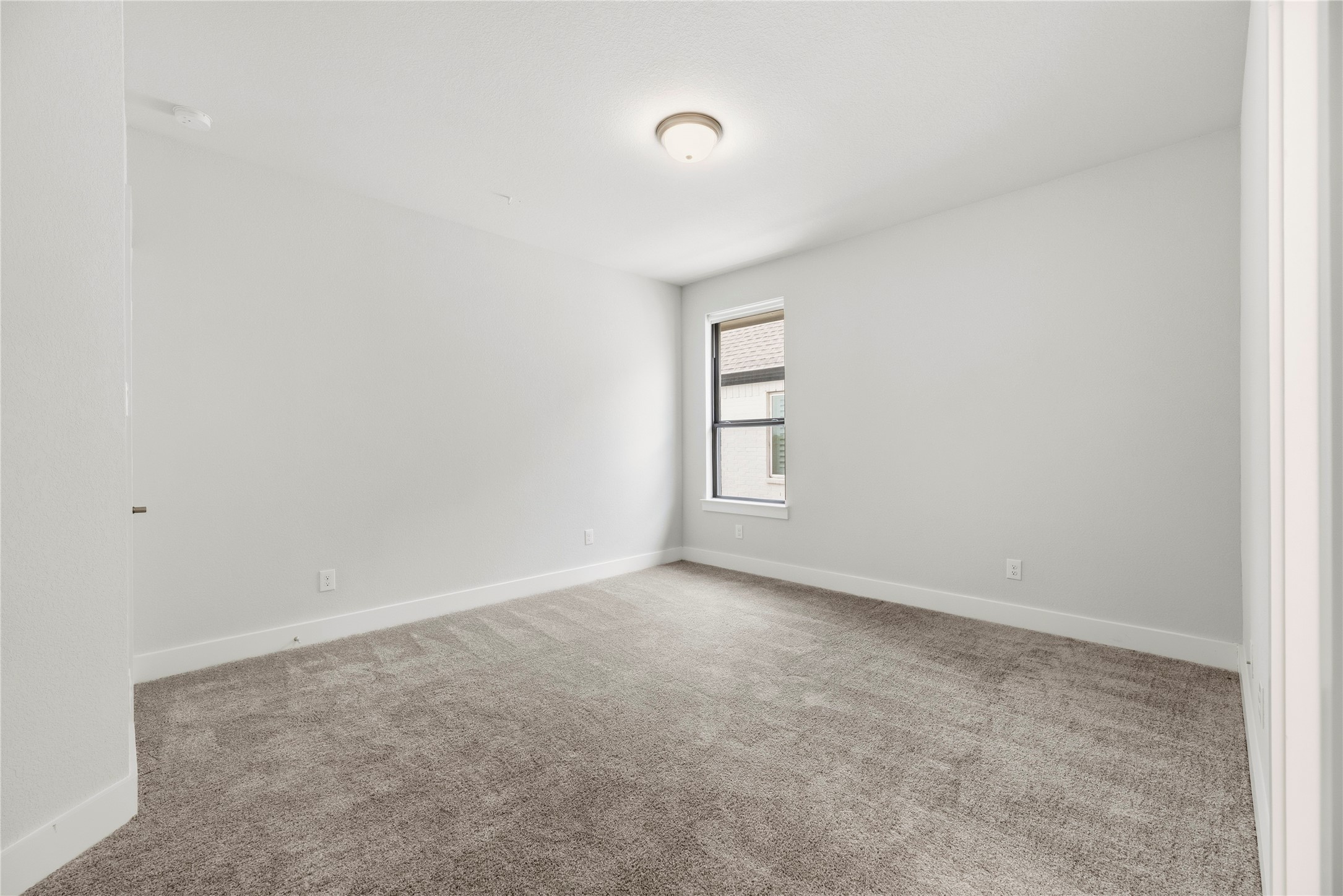 Move-in ready bedroom featuring neutral walls, soft carpet, and a large window overlooking the side property.