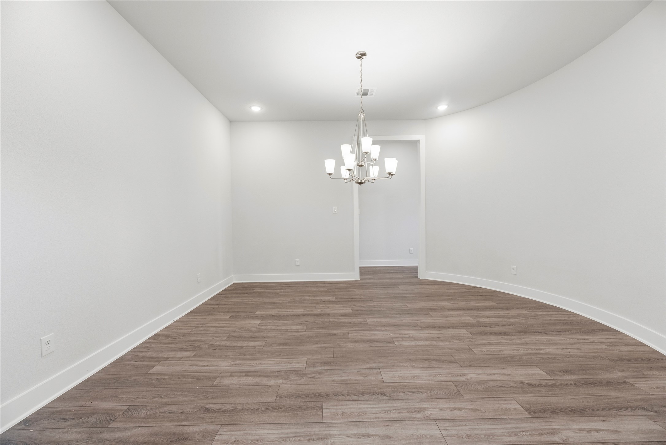 Elegant dining area showcasing a multi-light chandelier, smooth wood-look plank flooring, and a subtle curved architectural accent wall.